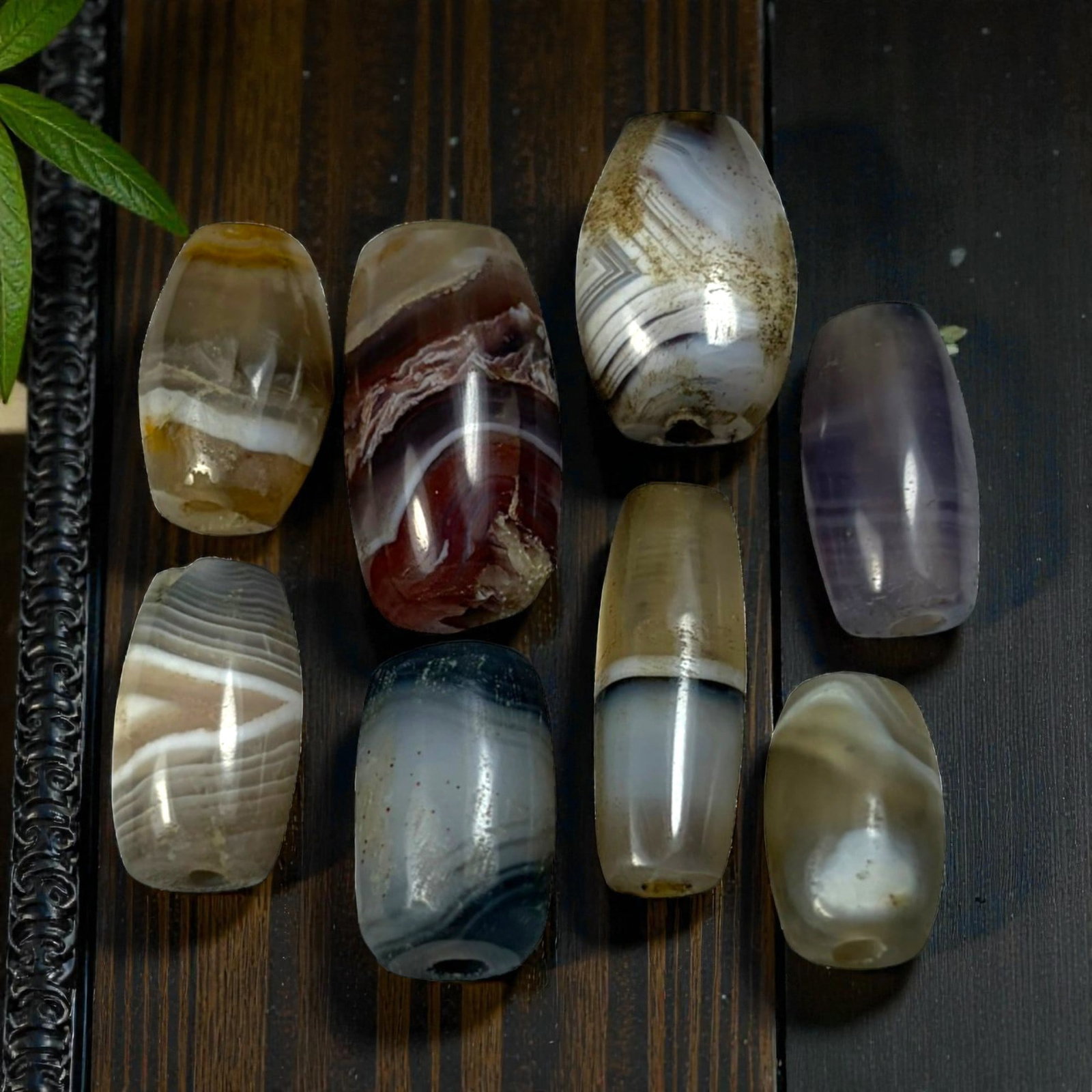 A Lot of 9 Himalayan Banded Agate Beads, Ancient to Antique Period, 54AN: Comprising lot of barrel and ovoid beads, each carved from banded agate with natural tonal variations, many displaying characteristic concentric, linear, and dendritic patterns. The surfaces exhibit s