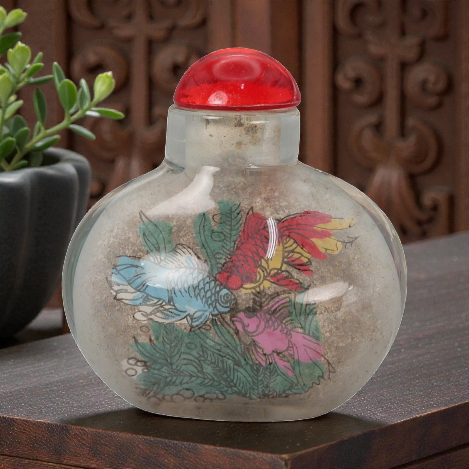 A Chinese Glass Snuff Bottle with Painted Decoration, 20th Century, 57FD: Formed from clear glass with a rounded flattened body and a short cylindrical neck, fitted with a domed red stopper. The interior is hand-painted with polychrome decoration depicting birds and floweri