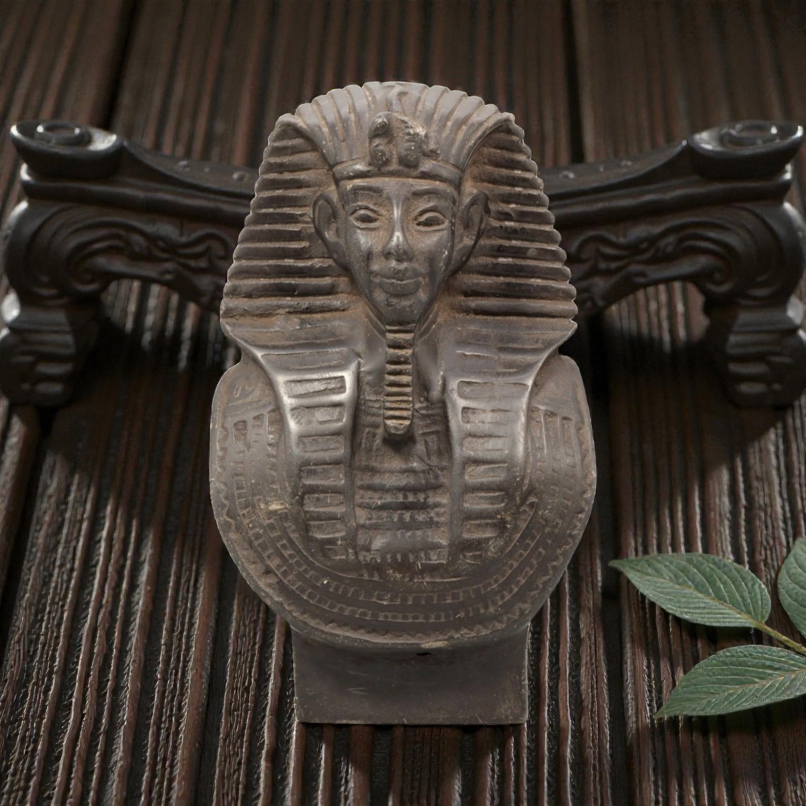 An Egyptian Revival Stone or Composite Bust, 20th Century, 94YC: Carved or cast in a dark-toned stone or stone-like composite material, the object is formed as a stylized bust representing an ancient Egyptian pharaoh. The figure wears a striated nemes headdress wit