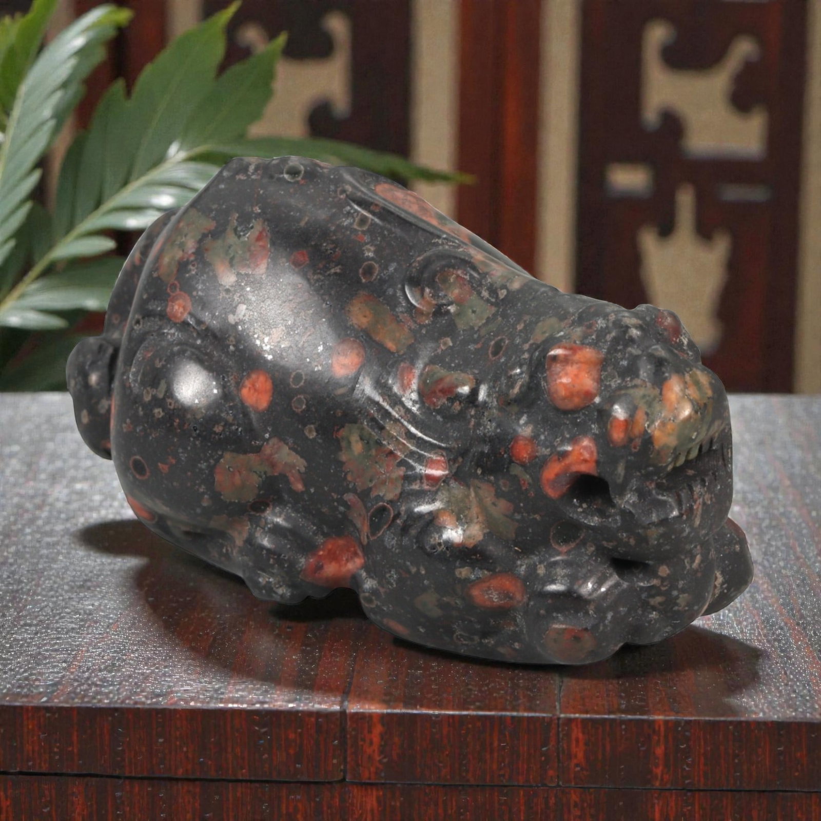 A Chinese Hardstone Carving of a Recumbent Mythical Beast, 20th Century, 91YA: Carved from dense dark hardstone with scattered russet and ochre inclusions, the figure is modeled as a compact recumbent mythical beast with a broad head and rounded body. The animal is shown crouchi