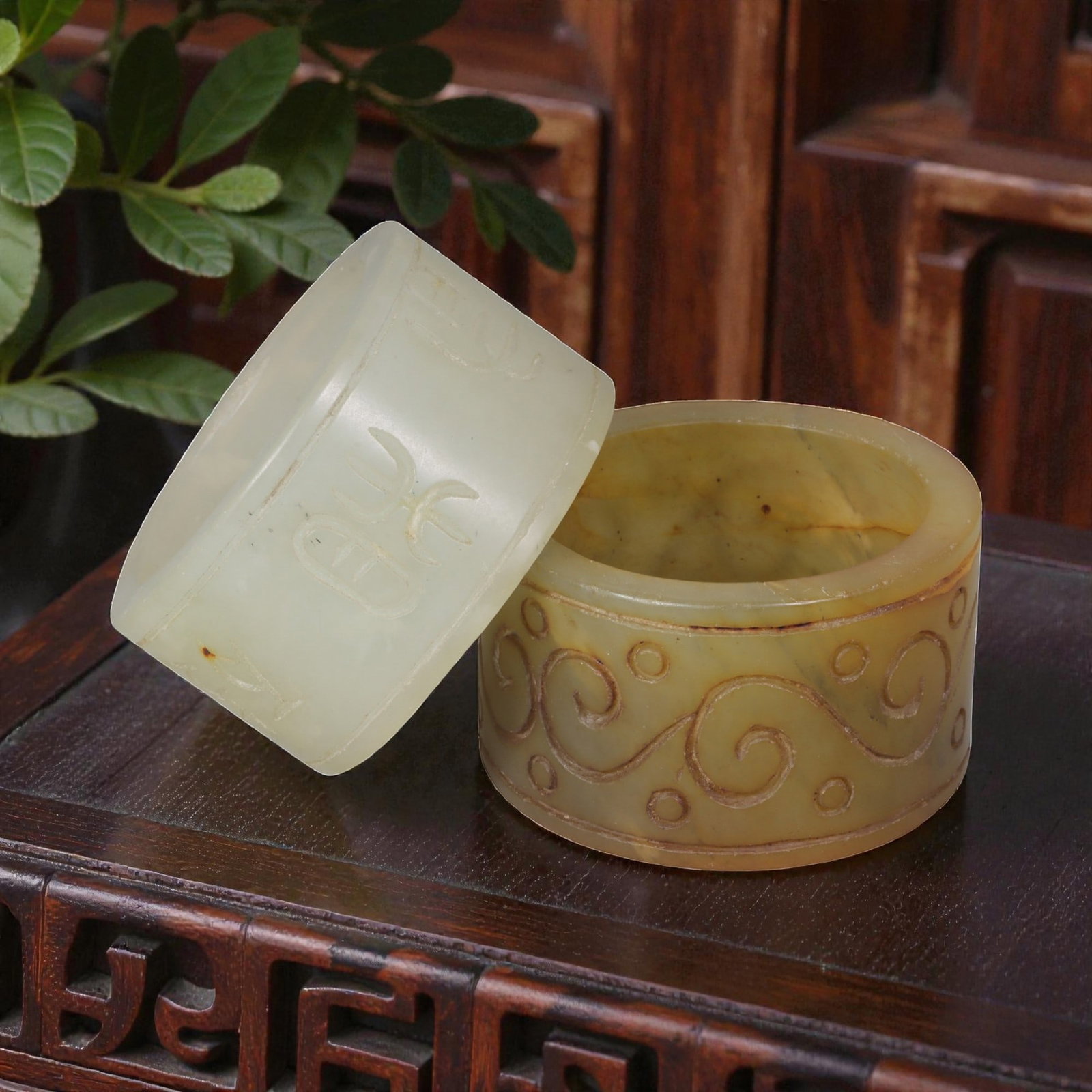 Lot of 2 Chinese Hetian Nephrite Jade Thumb Rings, 56AG: Carved from nephrite jade with natural color variations, the two cylindrical pendants feature incised decoration. The left example is pale, translucent jade with stylized archaic script characters etc