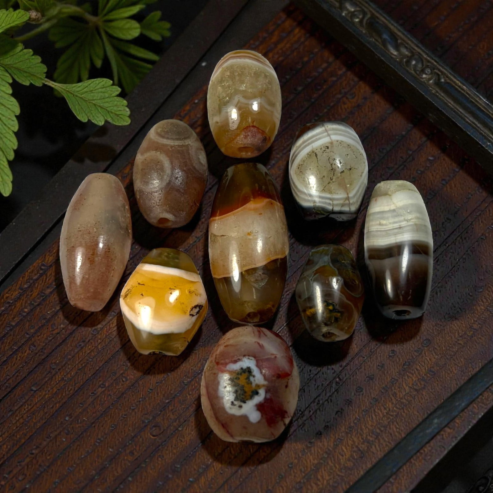 A Lot of 9 Himalayan Banded Agate Beads, Ancient to Antique Period, 46AN: Comprising lot of barrel and ovoid beads, each carved from banded agate with natural tonal variations, many displaying characteristic concentric, linear, and dendritic patterns. The surfaces exhibit s