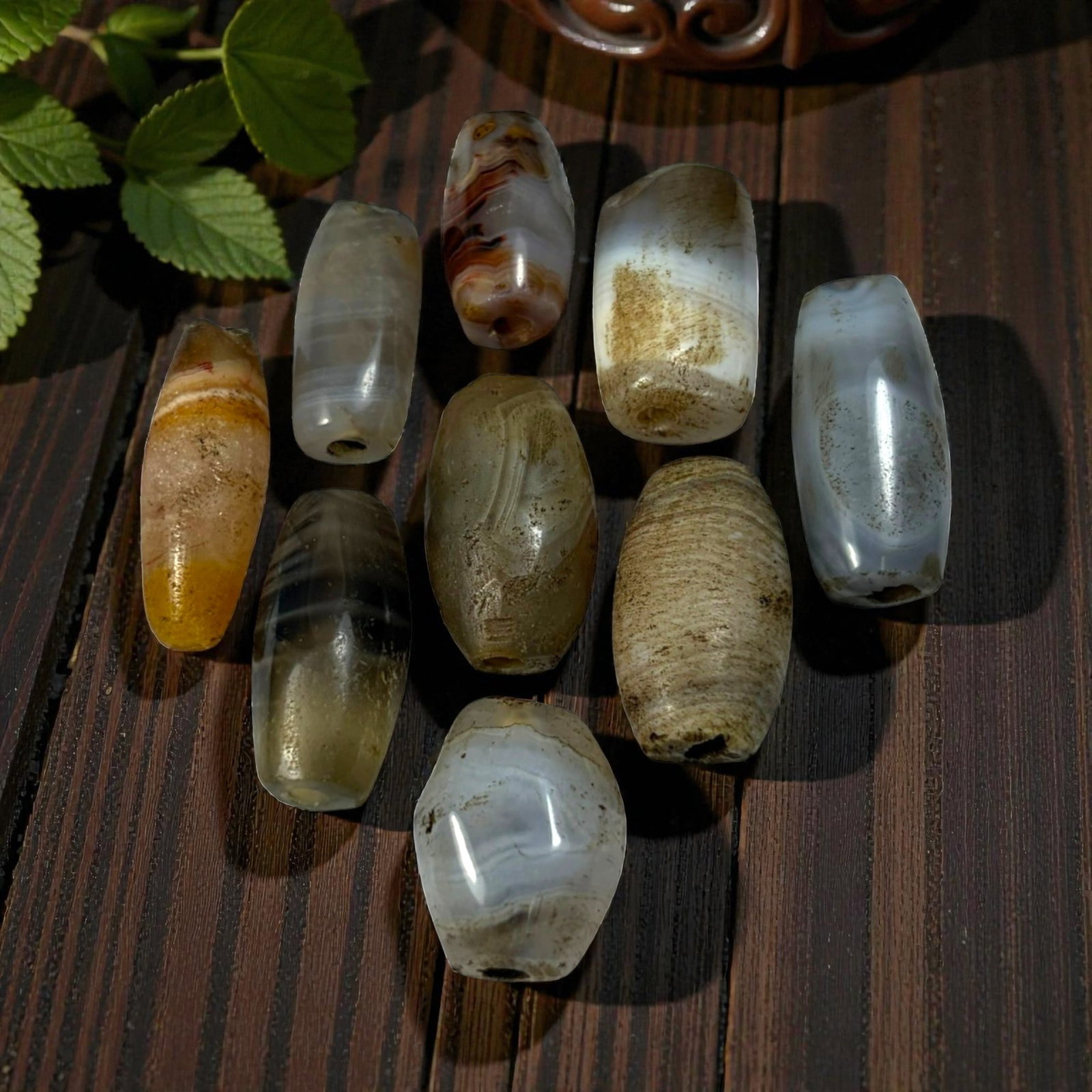 A Lot of 9 Himalayan Banded Agate Beads, Ancient to Antique Period, 52AN: Comprising lot of barrel and ovoid beads, each carved from banded agate with natural tonal variations, many displaying characteristic concentric, linear, and dendritic patterns. The surfaces exhibit s