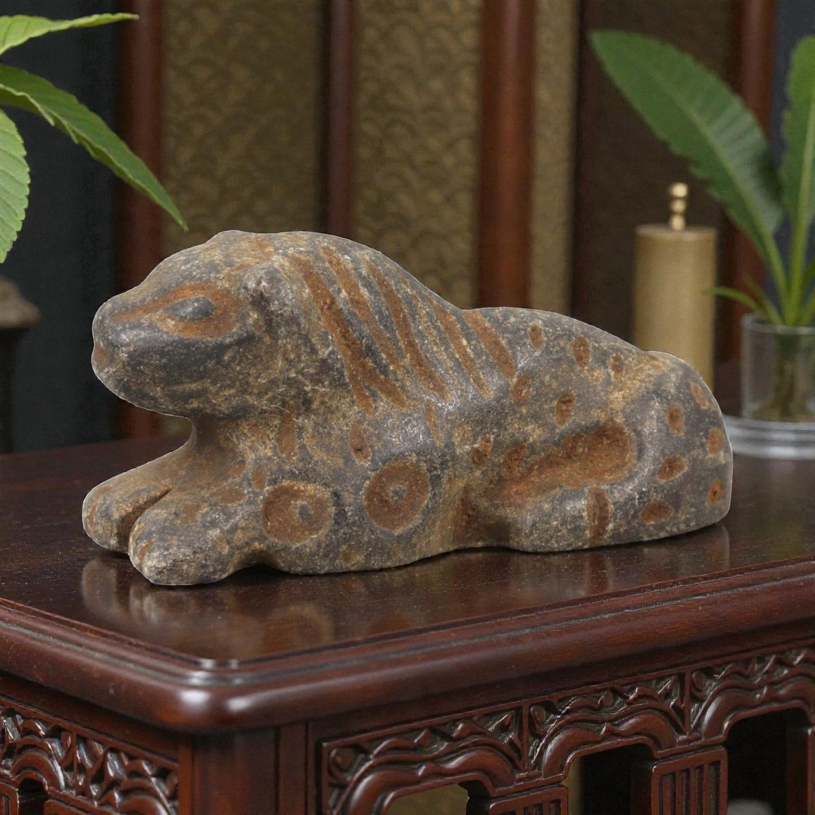Ancient Stone Zoomorphic Amulet - Near Eastern Feline Figure, 12AM: This amulet is carved from dark stone, depicting a recumbent feline in a crouched posture, with incised linear and circular motifs defining the mane, spots, and facial features. The piece reflects the