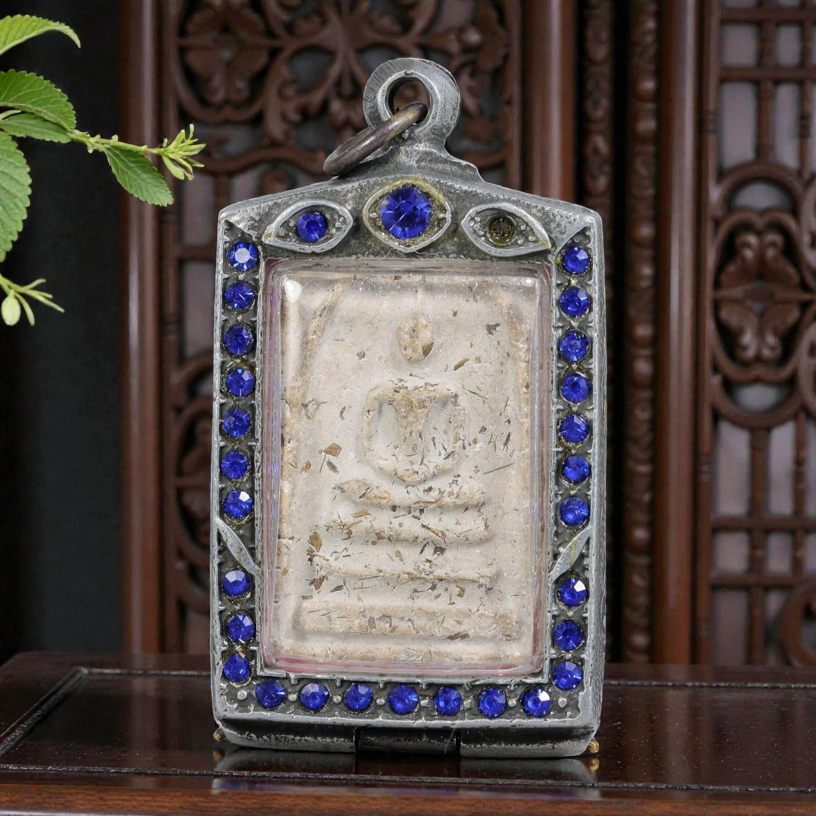 Thai Phra Somdej Amulet - Blue Crystal Silver Tone Pendant, 61ZB: A Thai Buddhist Phra Somdej amulet featuring a seated Buddha figure on tiered bases, housed in a silver-tone metal casing with blue crystal detailing. The glass-fronted enclosure protects the aged amu