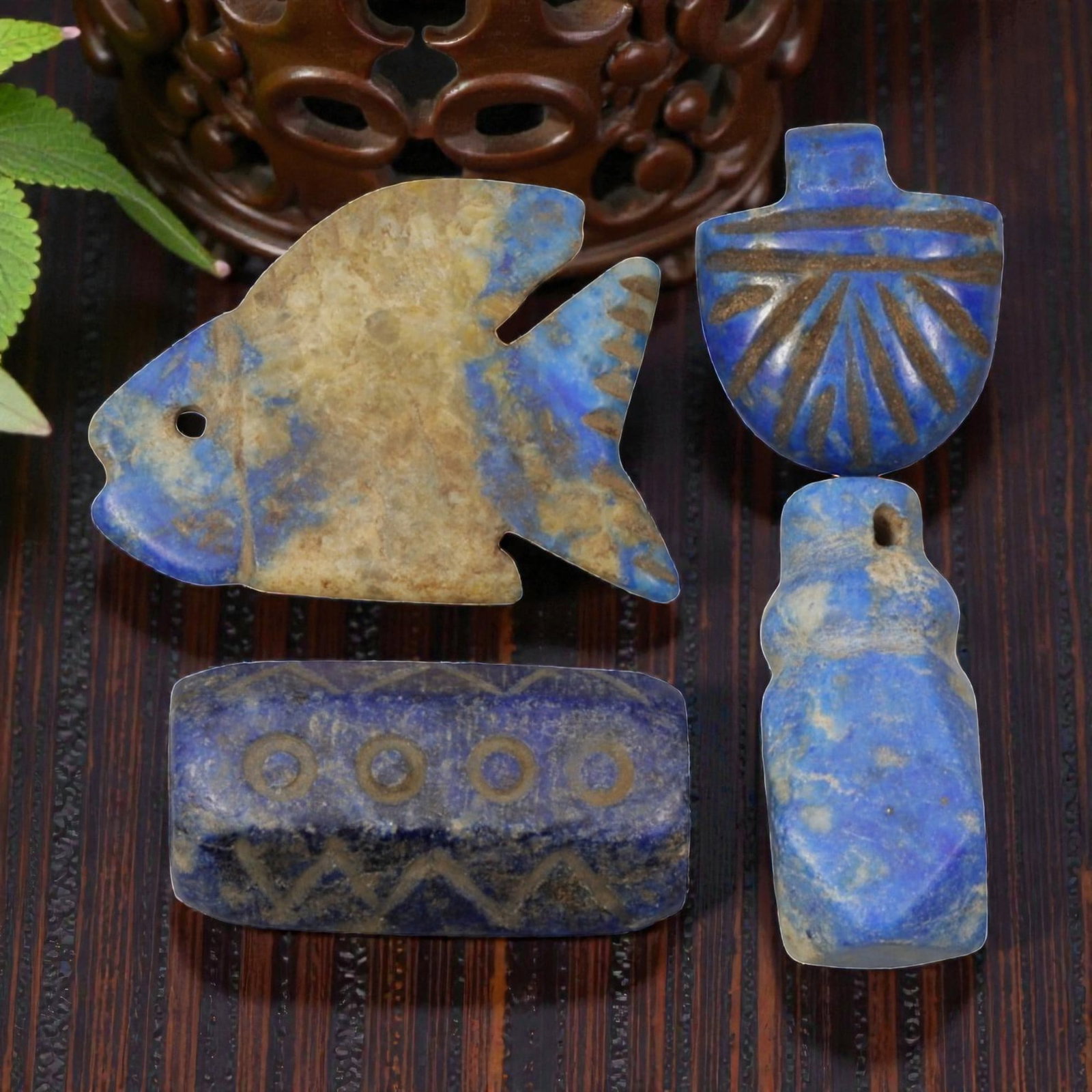 Lot of 4 Ancient Parthian Lapis Lazuli Amulets, 49WM: The group comprises four amulets carved from lapis lazuli, exhibiting natural blue coloration with inclusions and surface patina. The forms include a stylized fish with a suspension hole, a rectangula