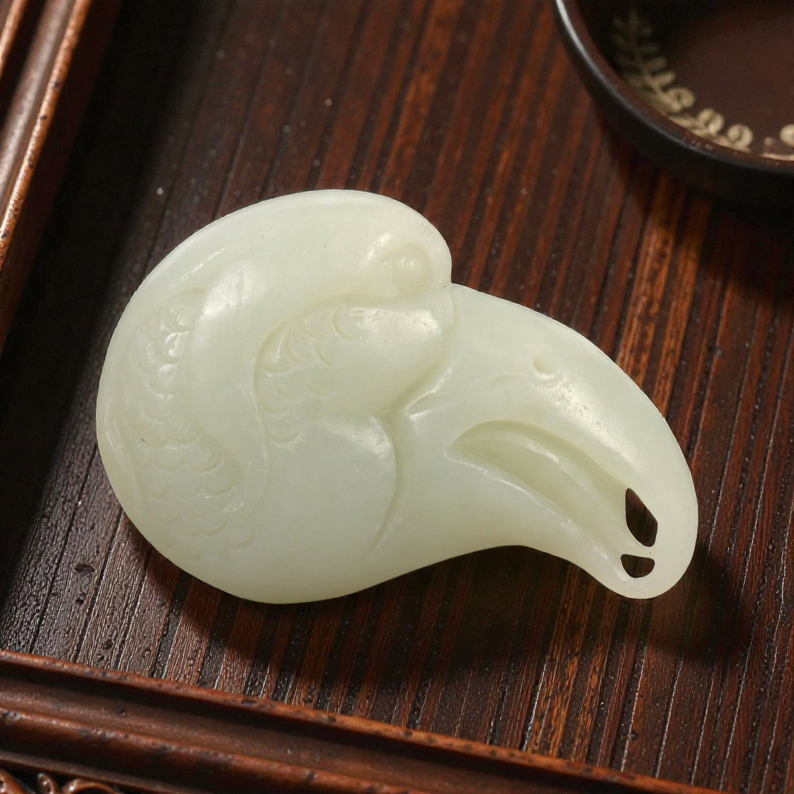 A Chinese Hetian Nephrite Jade Bird-Head Pendant, 20th Century, 30FA: Carved from pale celadon nephrite jade with even translucency and minor natural inclusions, the object is worked in the form of a stylized bird's head shown in profile. The rounded cranial form transi