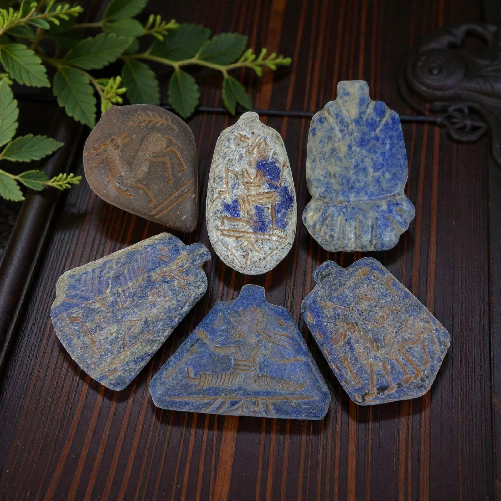 A Lot of 6 Ancient Near Eastern Lapis Lazuli Amulets, 10AC: The group comprises six amulets, five carved from lapis lazuli and one from a brown stone, exhibiting varied tones and natural mineral inclusions, alongside surface patina and wear consistent with ant