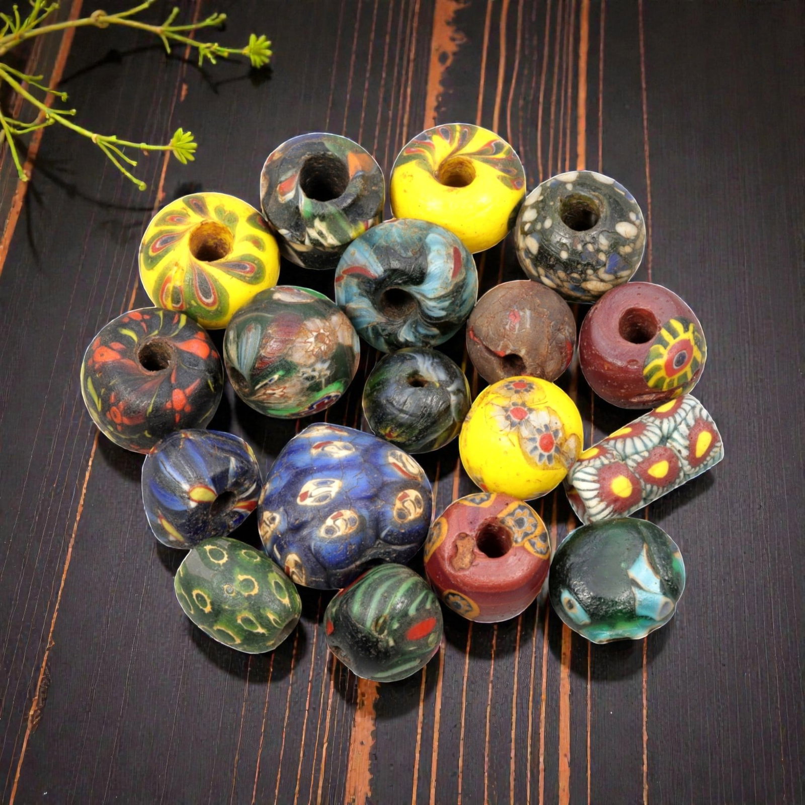 A Lot of 17 Antique/ Vintage Artisan Glass Trade Beads, 26WM: A curated collection of 17 glass trade beads, varying in form from spherical, barrel, and cylindrical to polygonal, all with central perforations. The beads feature intricate mosaic, trailed, and appl