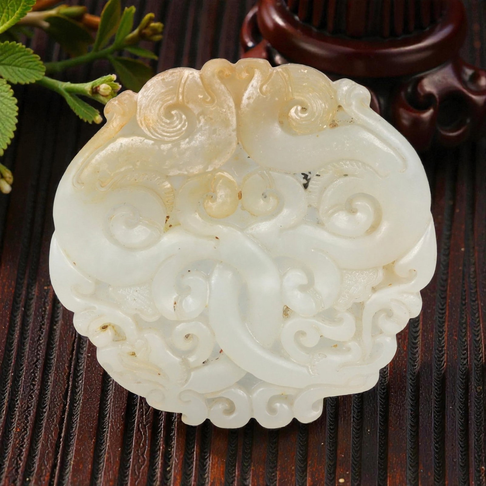 A Chinese Hetian Jade Cloud-Form Plaque, 20th Century, 68FH: Carved from pale celadon Hetian nephrite jade with soft translucency and scattered natural inclusions, the plaque is worked as a rounded form with a gently lobed outline. The surface is carved in low 