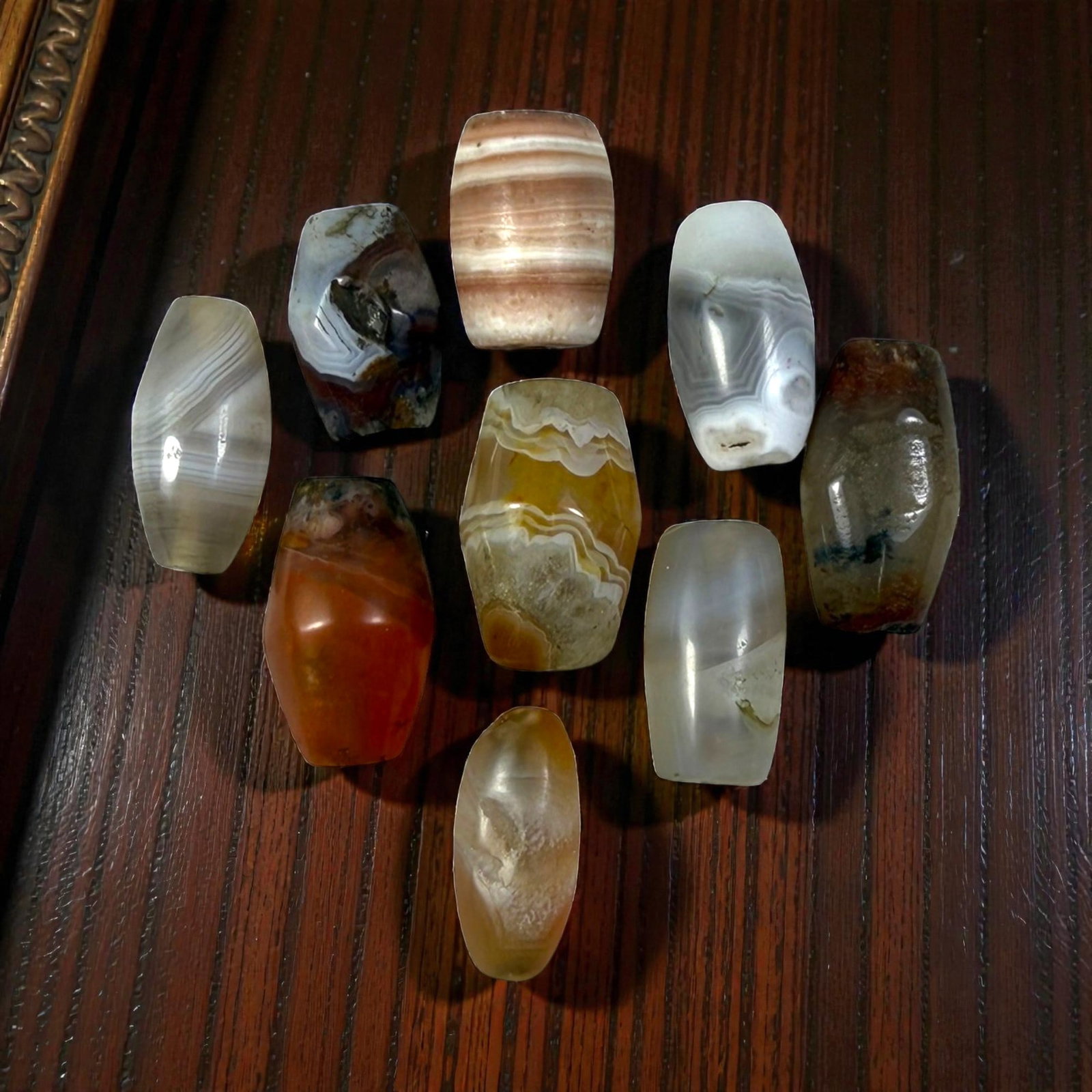 A Lot of 9 Himalayan Banded Agate Beads, Ancient to Antique Period, 15YD: Comprising lot of barrel and ovoid beads, each carved from banded agate with natural tonal variations, many displaying characteristic concentric, linear, and dendritic patterns. The surfaces exhibit s