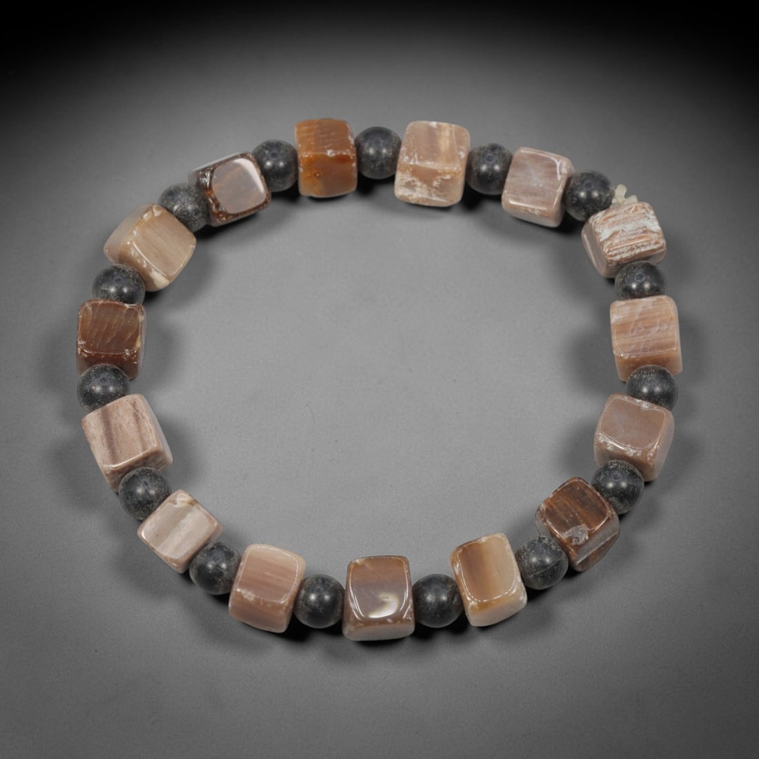 A Fossilised Wood Square Bead Bracelet With Dark Round Stone Spacers, 34ZK: An artisanal hand-strung bracelet constructed from polished square-cut fossilised wood beads, interspersed with smooth dark round mineral spacer beads to create balanced structure. The fossil wood bea