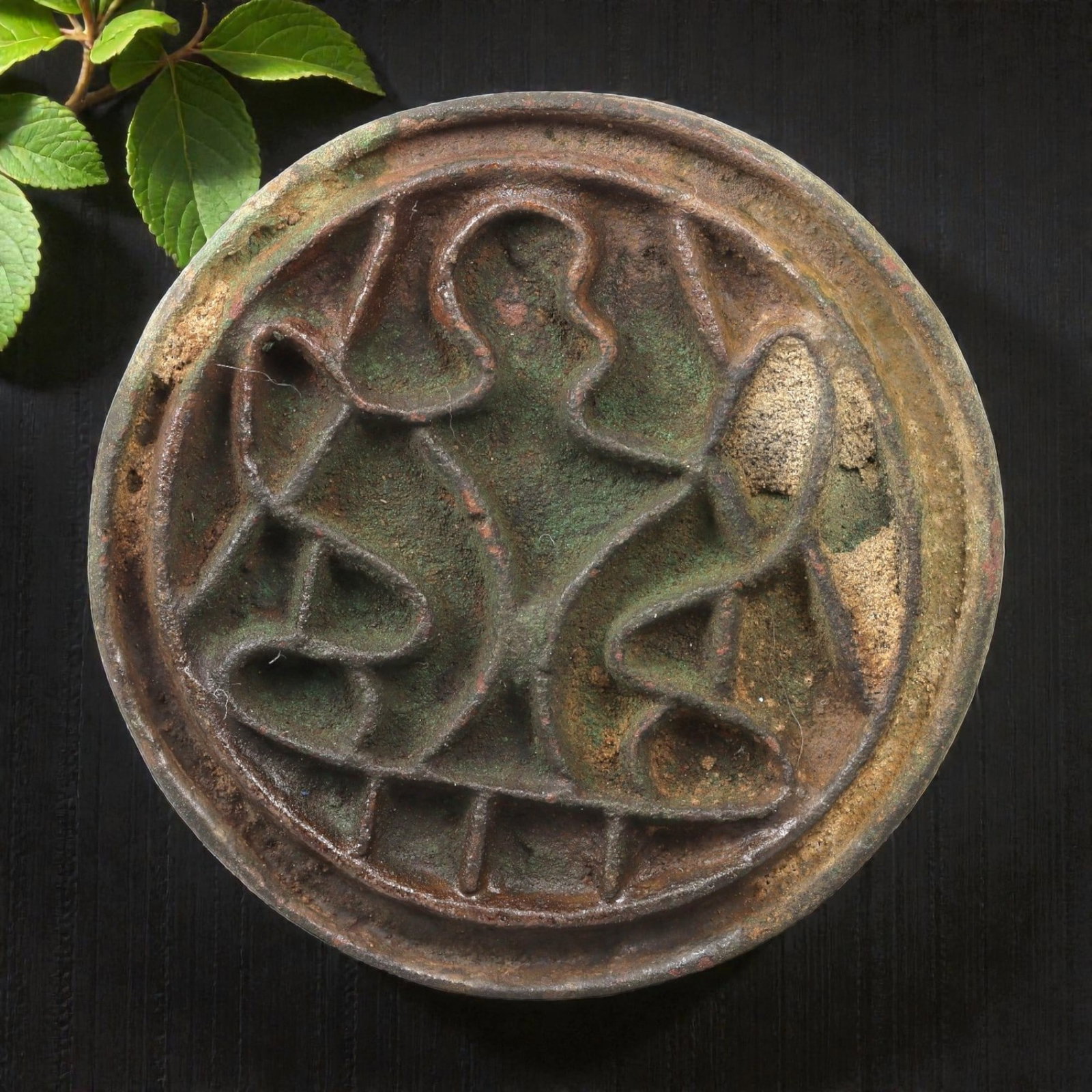 An Ancient Bactrian Bronze Stamp Seal, 54AG: A circular bronze stamp seal of the Bactrian period, with a raised relief design depicting a stylized central motif flanked by curvilinear elements, framed within a double border. The surface displays