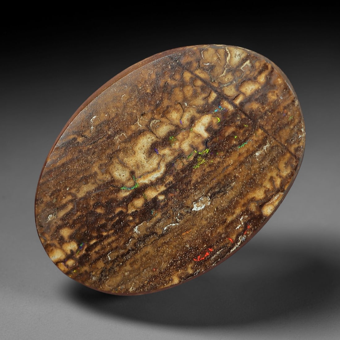 1.95 Carats Brown Matrix Multicolor Koroit Yowah Opal Cabochon - Natural Australian Stone, 21XM: This singular Koroit Yowah opal cabochon presents a striking natural tableau, with a rich brown ironstone matrix interwoven with delicate veins and flecks of iridescent opal. The stone's oval form sho