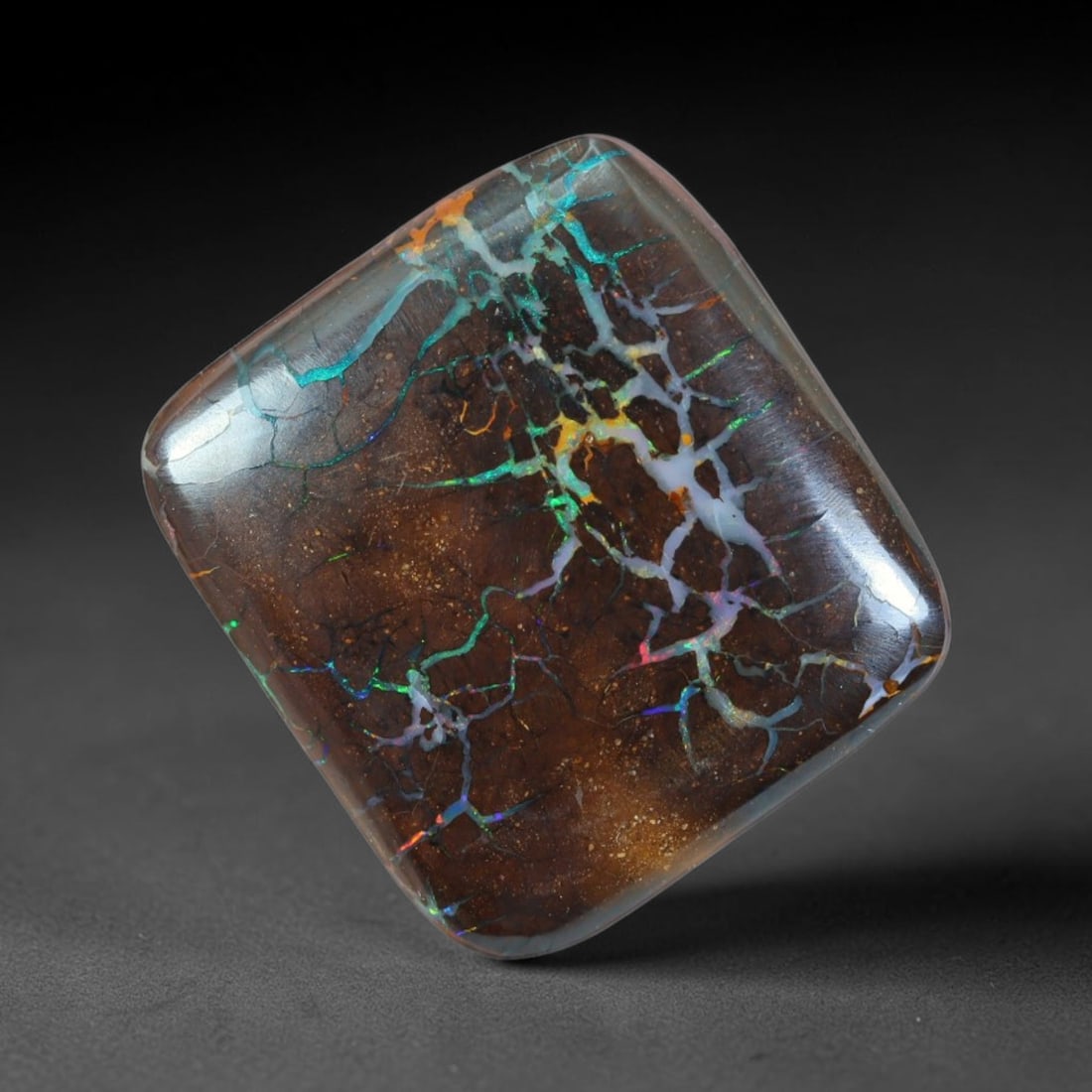 23.33ct Natural Australian Queensland Matrix Boulder Opal Cabochon, 77AT: Hand polished rounded square cushion cabochon of natural Queensland matrix boulder opal, set upon rich dark ironstone matrix threaded with intricate web-like opal veins displaying cyan, emerald green,
