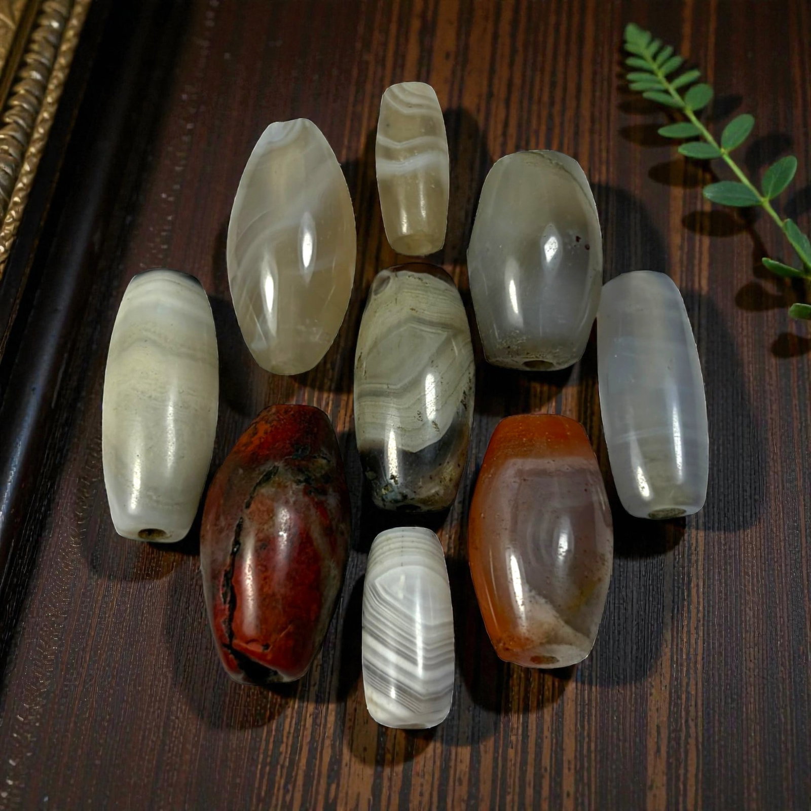 A Lot of 9 Himalayan Banded Agate Beads, Ancient to Antique Period, 42AN: Comprising lot of barrel and ovoid beads, each carved from banded agate with natural tonal variations, many displaying characteristic concentric, linear, and dendritic patterns. The surfaces exhibit s