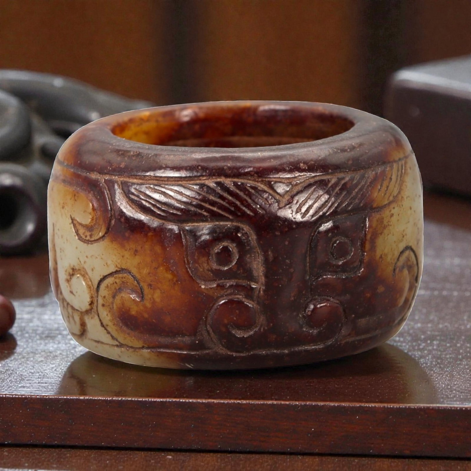 A Chinese Nephrite Jade Ring, 20th Century, 13FA: Carved from mottled brown and pale celadon nephrite jade with natural color variation and areas of translucency, the ring is formed with a thick circular profile and a wide band. The exterior surface 