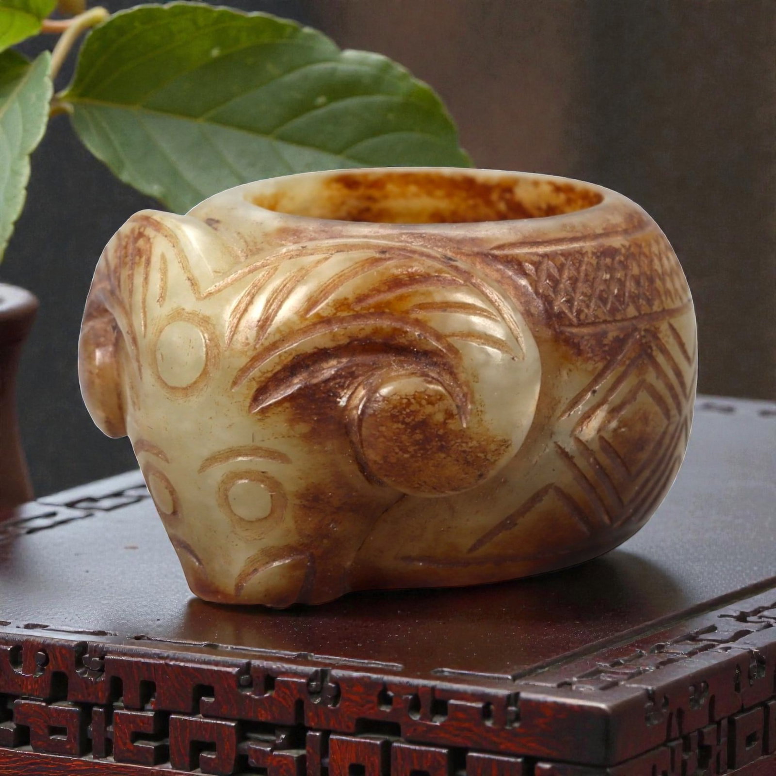 A Chinese Nephrite Jade Ram-Head Ring, 14FA: Carved from mottled celadon and russet-toned nephrite jade with natural color variation and areas of translucency, the ring is formed with a sculptural ram's head projecting from the bezel. The head i