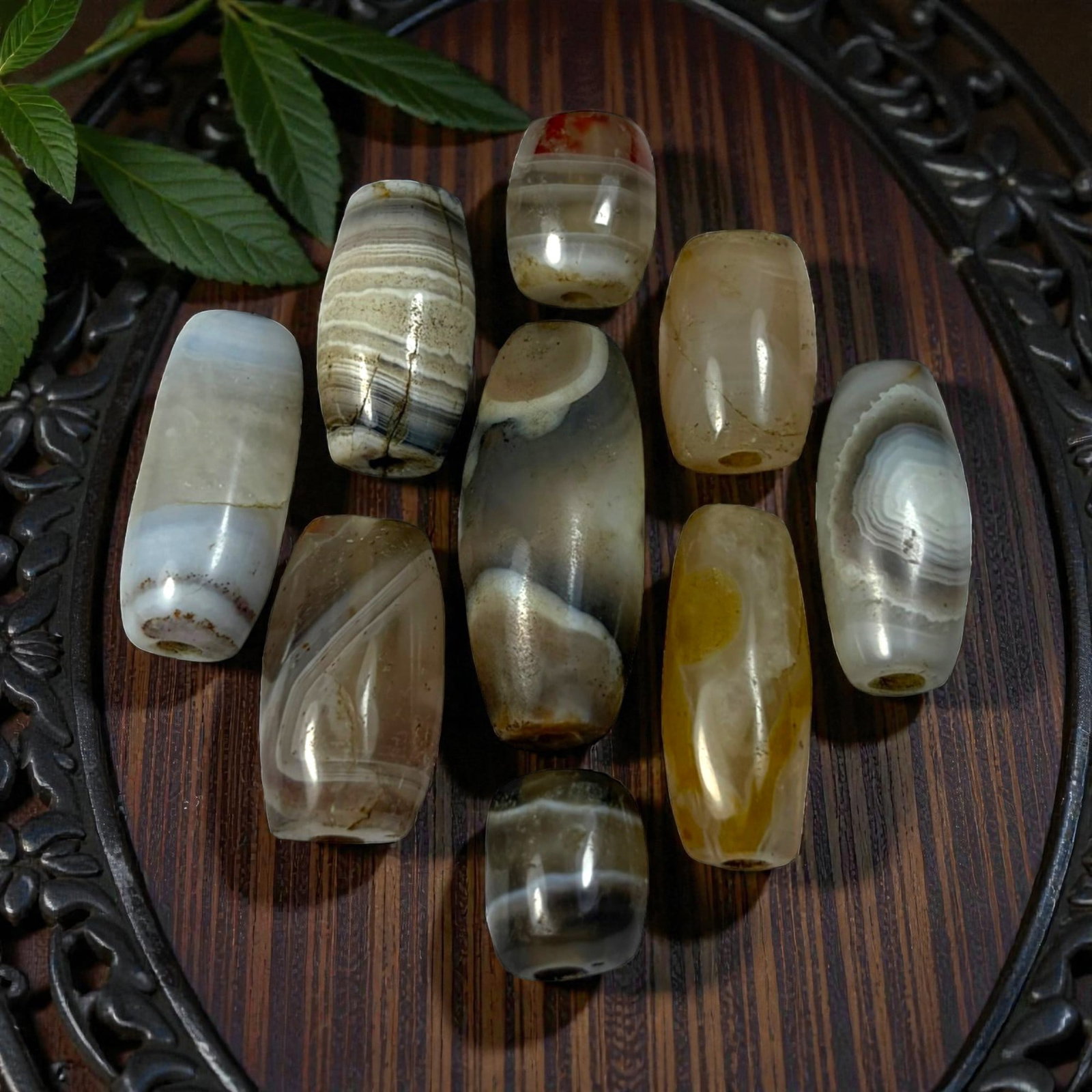 A Lot of 9 Himalayan Banded Agate Beads, Ancient to Antique Period, 43AN: Comprising lot of barrel and ovoid beads, each carved from banded agate with natural tonal variations, many displaying characteristic concentric, linear, and dendritic patterns. The surfaces exhibit s