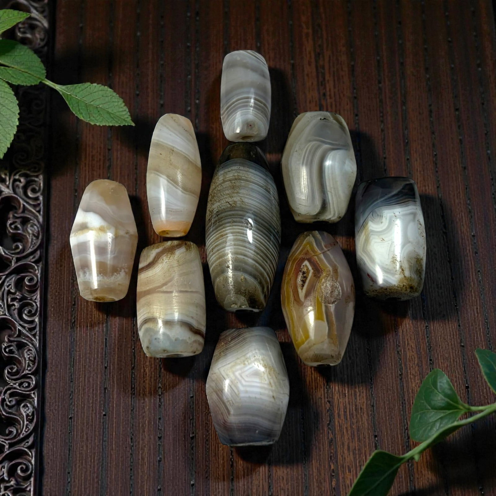 A Lot of 9 Himalayan Banded Agate Beads, Ancient to Antique Period, 41AN: Comprising lot of barrel and ovoid beads, each carved from banded agate with natural tonal variations, many displaying characteristic concentric, linear, and dendritic patterns. The surfaces exhibit s