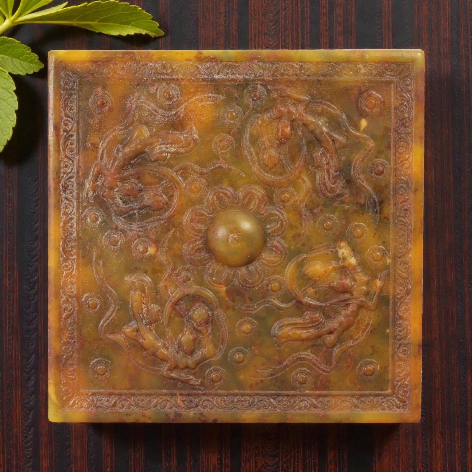 A Chinese Jade Relief Plaque, 20th Century, 50FD: Carved from mottled yellow-brown and olive-toned jade with areas of natural translucency and darker inclusions. The plaque is square in form and worked in shallow to moderate relief on one face, frame