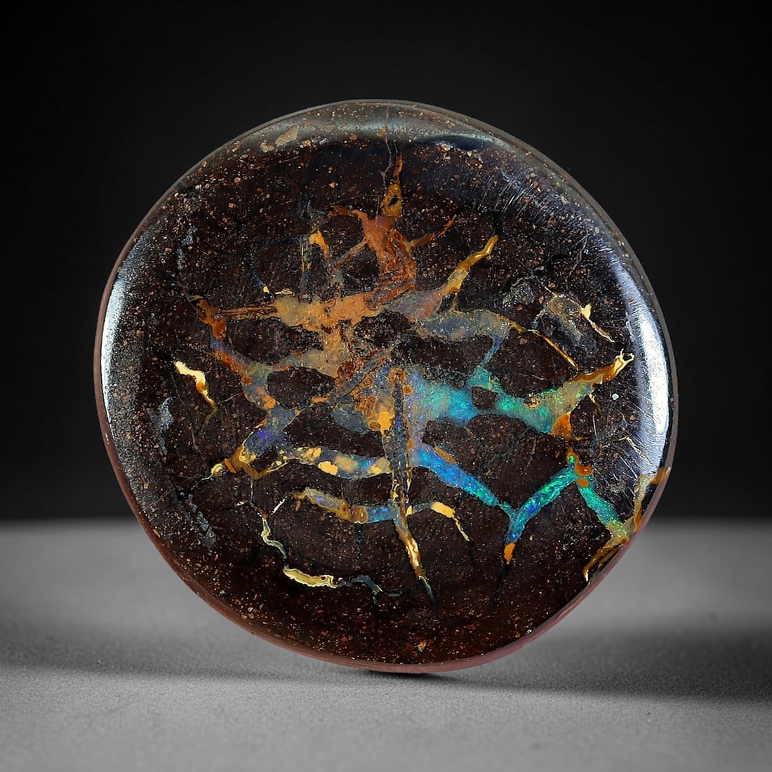 6.86ct Natural Australian Queensland Matrix Boulder Opal Cabochon, 23AV: Hand polished smooth round cabochon of natural Queensland matrix boulder opal, featuring dark speckled ironstone host matrix woven with interlaced warm golden amber opal veins paired with striking swa