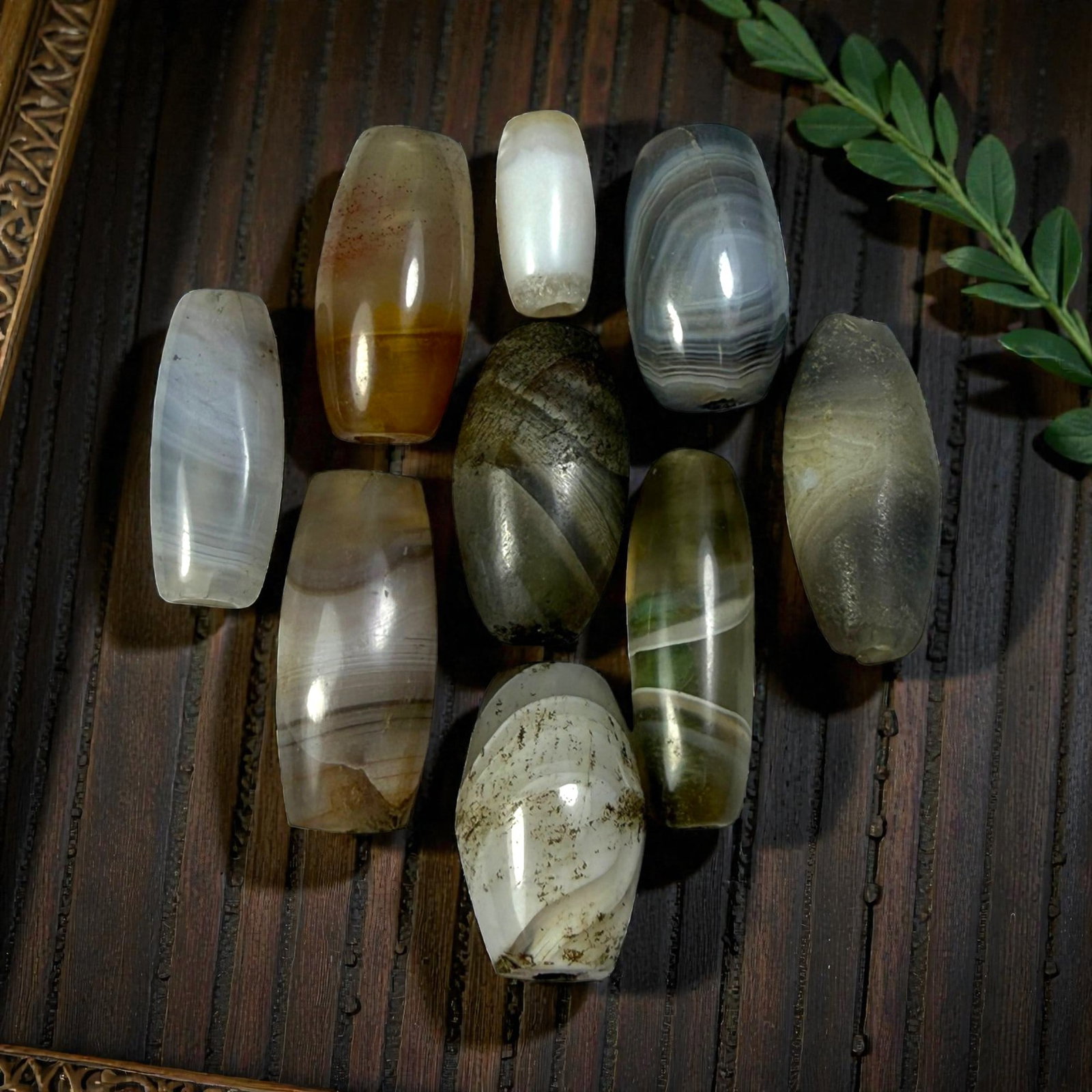 A Lot of 9 Himalayan Banded Agate Beads, Ancient to Antique Period, 50AN: Comprising lot of barrel and ovoid beads, each carved from banded agate with natural tonal variations, many displaying characteristic concentric, linear, and dendritic patterns. The surfaces exhibit s
