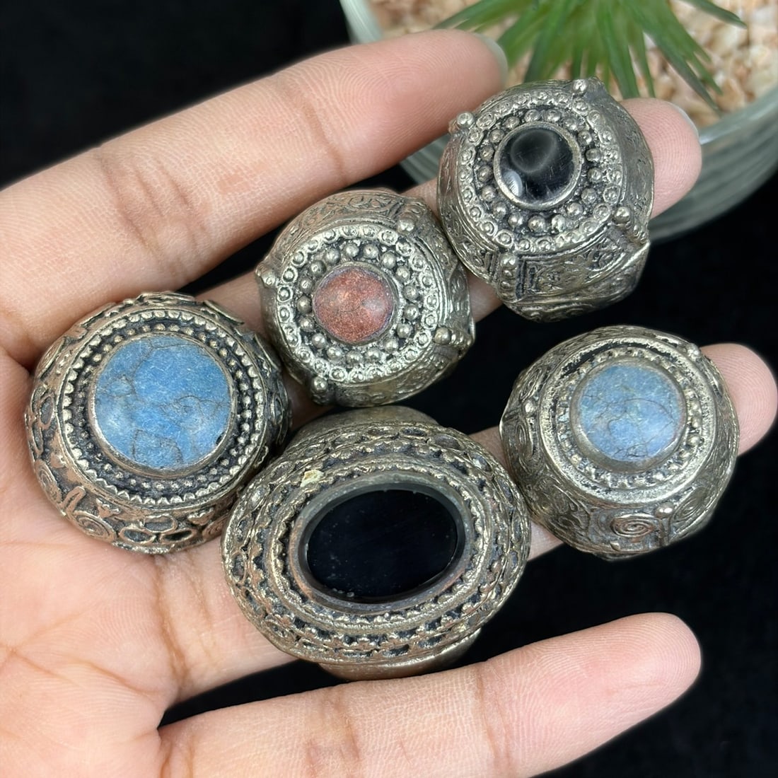 Vintage Tibetan Carved Silvered Mixed Mineral Inlay Rings Lot, 13AS: This set of five untested silvered alloy adjustable rings follows classic Tibetan tribal craft traditions, adorned with intricate hand-carved scroll motifs and layered granulation filigree encircling 