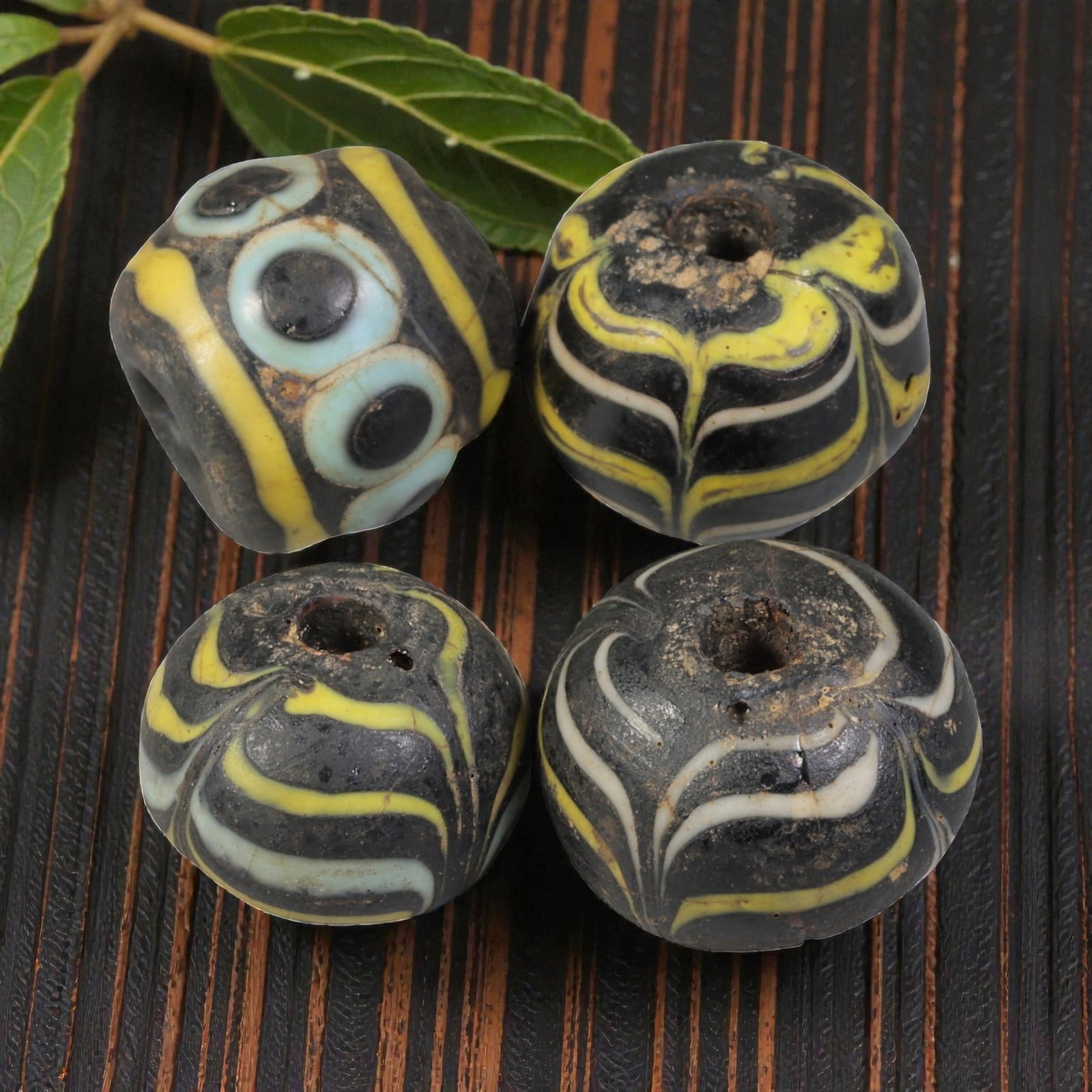 Lot of 4 Antique Islamic Feather & Eye-Patterned Glass Beads, Circa 9th-14th Century, 41WM: A group of four glass beads, varying in form from spherical to barrel-shaped, all with central perforations. The beads display two distinct decorative styles: feather-patterned trailed glass in contra