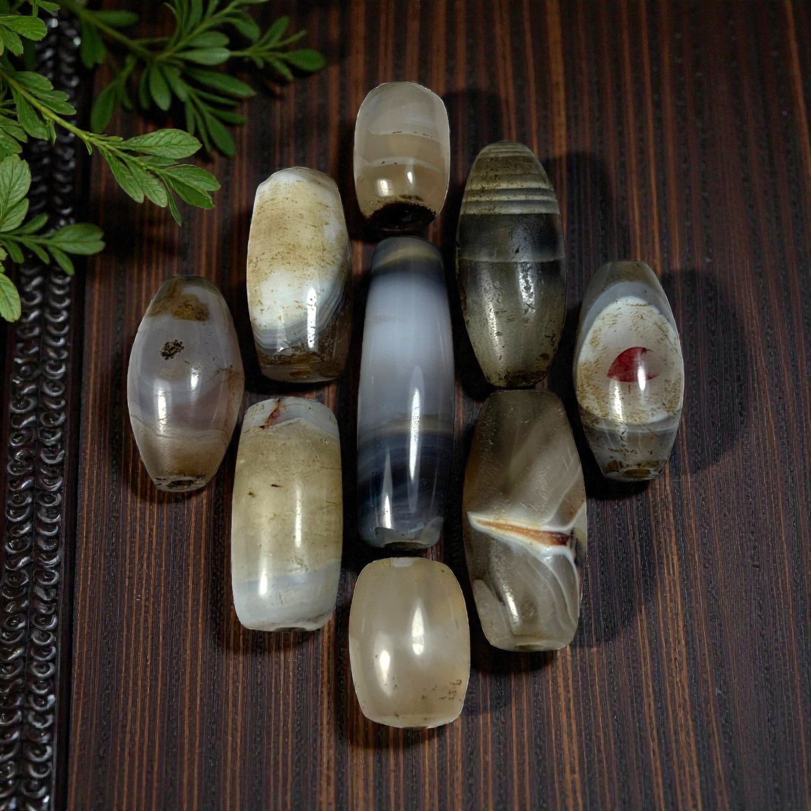 A Lot of 9 Himalayan Banded Agate Beads, Ancient to Antique Period, 40AN: Comprising lot of barrel and ovoid beads, each carved from banded agate with natural tonal variations, many displaying characteristic concentric, linear, and dendritic patterns. The surfaces exhibit s