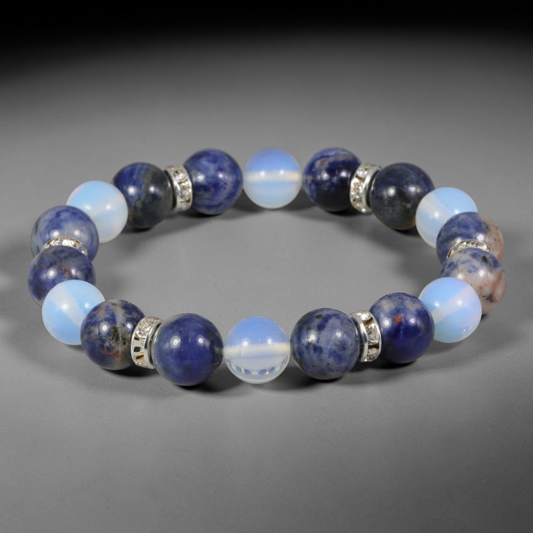 Natural Mixed Stone Beaded Bracelet - Polished Round Bead Strand, 52FA: This strand is composed of uniformly sized polished natural stone spherical beads interspersed with silvered metal spacer accents. The hard stone exhibits natural mineral veining, mottled inclusions a