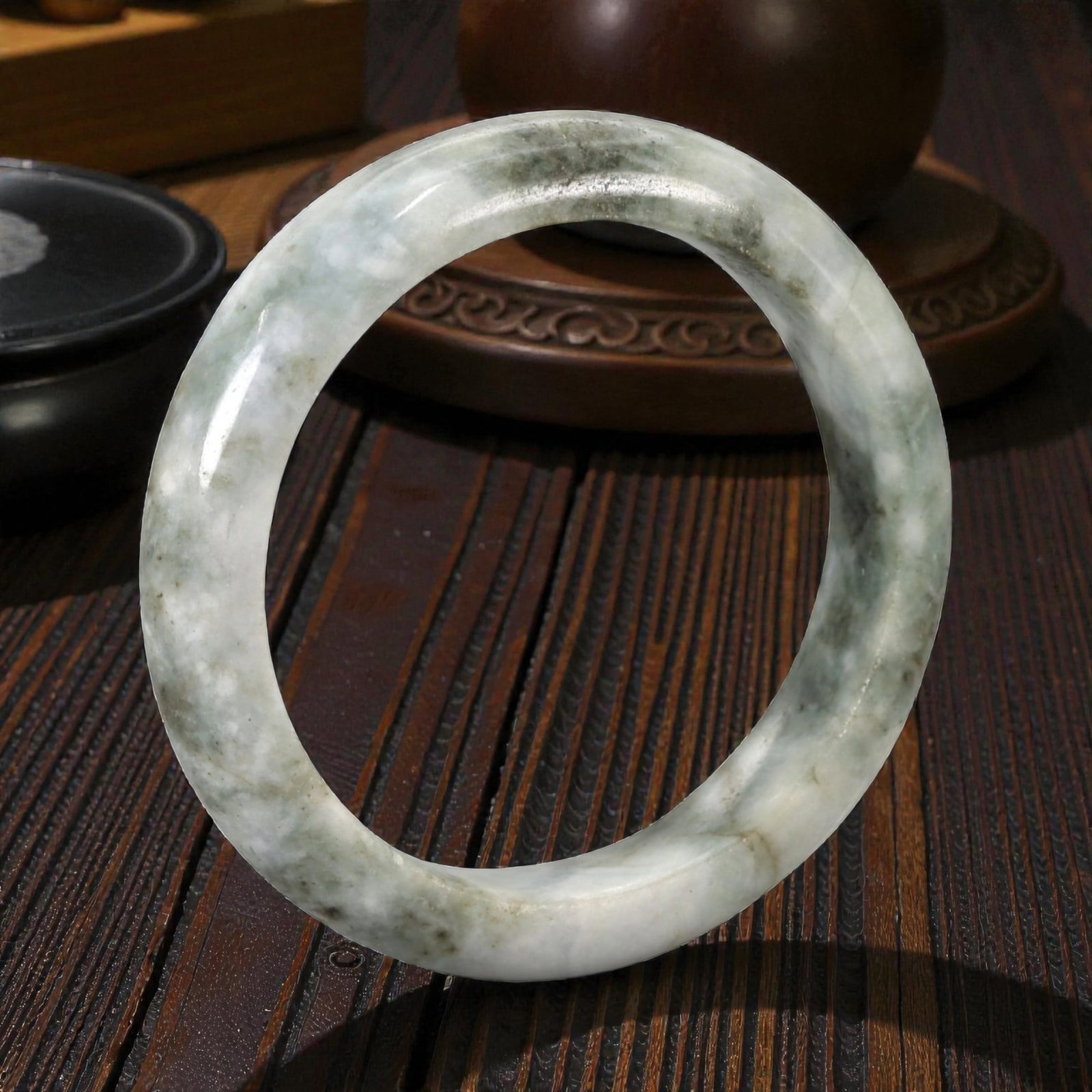 Natural Burmese Type A Jadeite Jade Bangle Bracelet, 20th Century, 92ZK: Carved from jadeite jade with a pale white base and irregular greyish-green mottling, the bangle is formed as a continuous circular band with a rounded cross-section. The surface is smoothly polished,