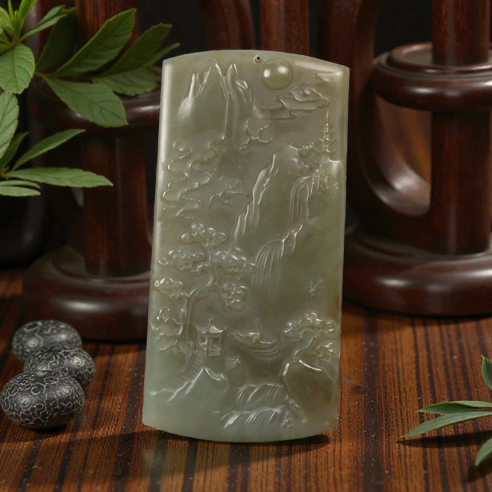 A Chinese Nephrite Jade Landscape Plaque Pendant, 81FC: Carved from pale celadon to grey-green nephrite jade with subtle tonal variation and minor natural inclusions, the object is worked as a vertically oriented plaque with a gently curved upper edge. The