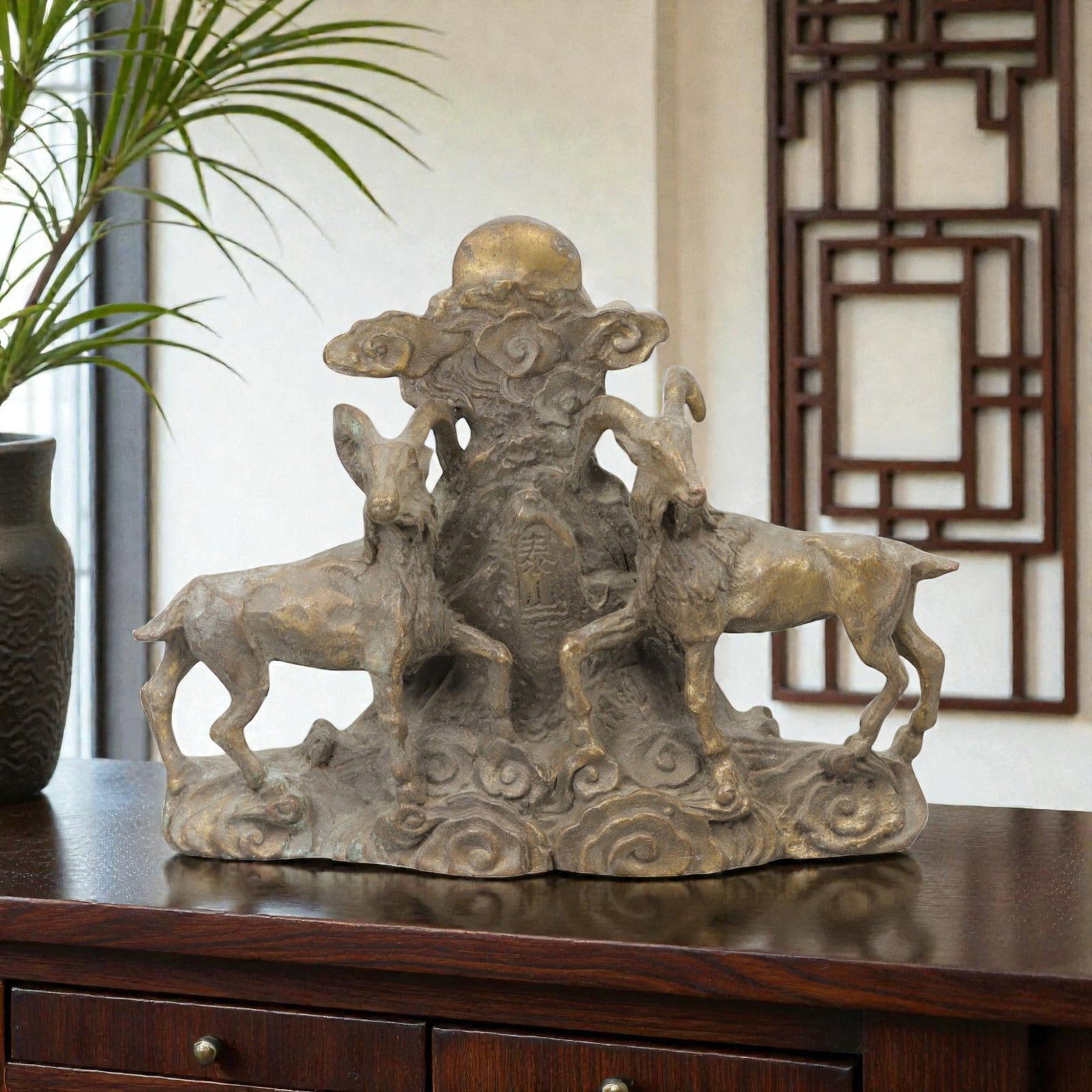 A Chinese Bronze Ram Group, 20th Century, 20FH: Cast in bronze with a dark brown surface and areas of lighter wear, the sculpture depicts a symmetrical group of two rams arranged on either side of a central vertical element. Each ram is shown stand