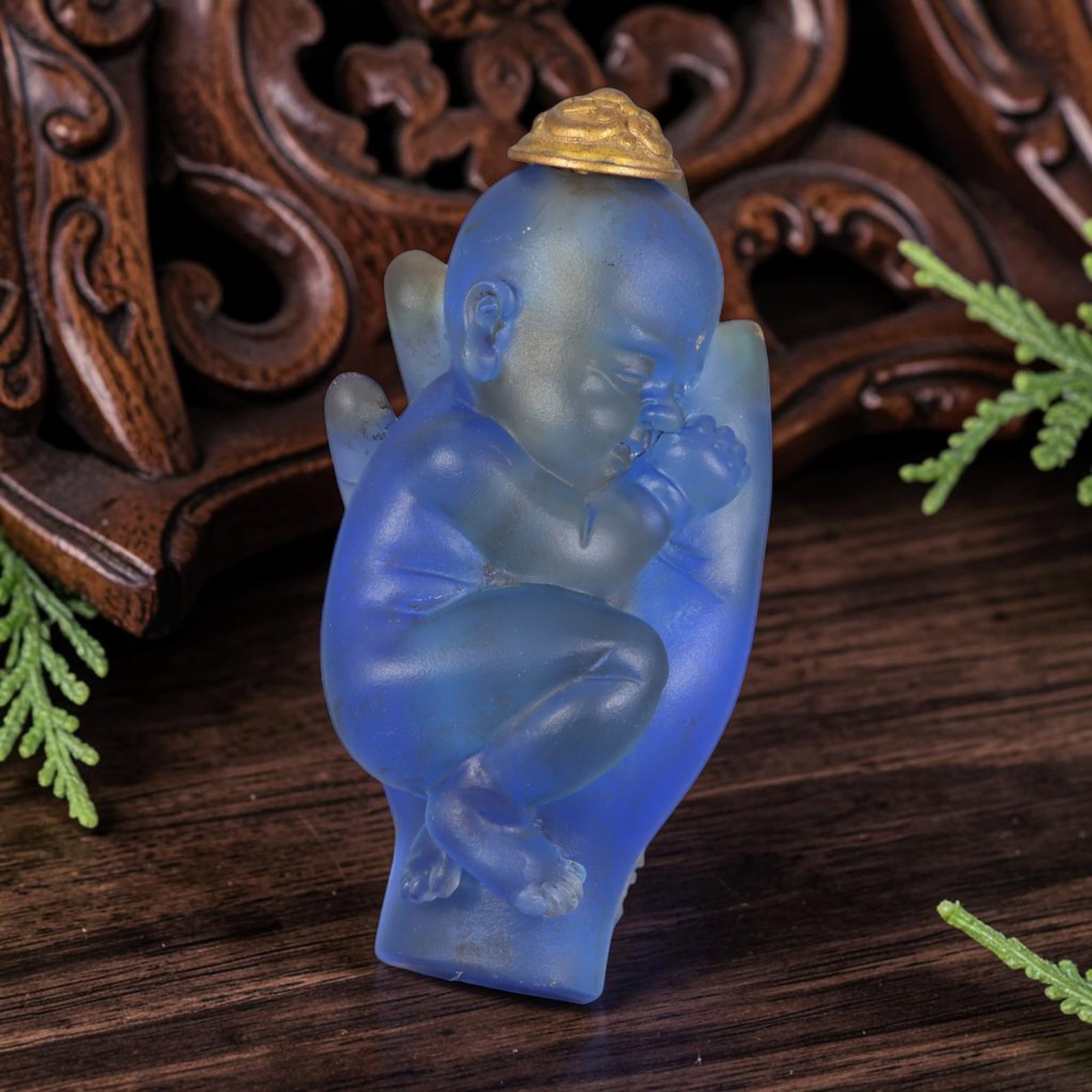 Vintage Chinese Liuli Glass Snuff Bottle - Baby in Deity Hand, 36AS: This snuff bottle is moulded from frosted translucent blue liuli glass, carved as a sleeping baby curled inside a Buddha hand, symbolizing divine protection. The piece features smooth rounded carving 