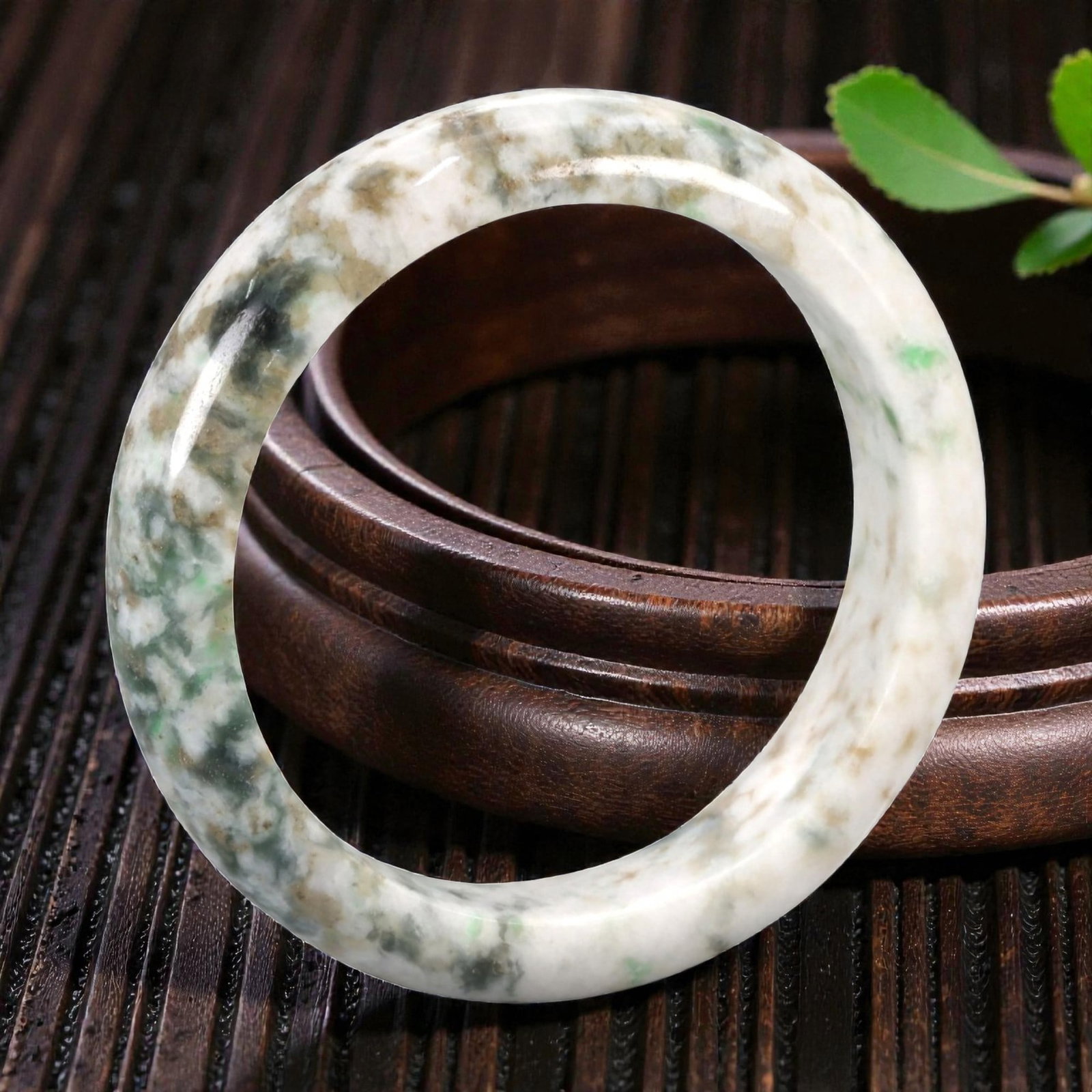 Natural Burmese Type A Jadeite Jade Bangle Bracelet, 20th Century, 80ZK: Carved from jadeite jade with a pale white base and irregular mottling of green, brown, and dark grey inclusions, the bangle is formed as a continuous circular band with a rounded cross-section. The s