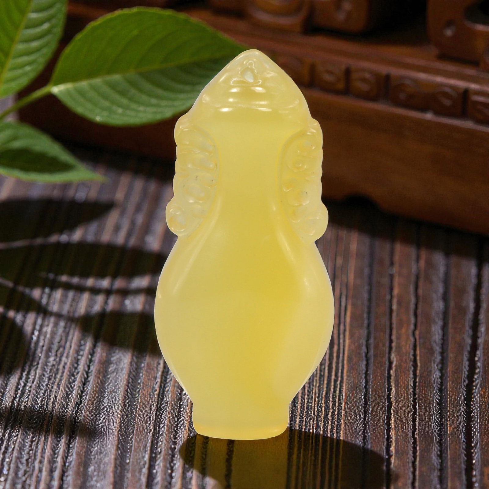 A Chinese Chalcedony or Yellow Jade Locket Pendant, 94FH: Carved from translucent yellow chalcedony with an even, softly diffused tone, the amulet is formed as a small locket-shaped vessel with a tapering neck and rounded body. The surface is smoothly polish