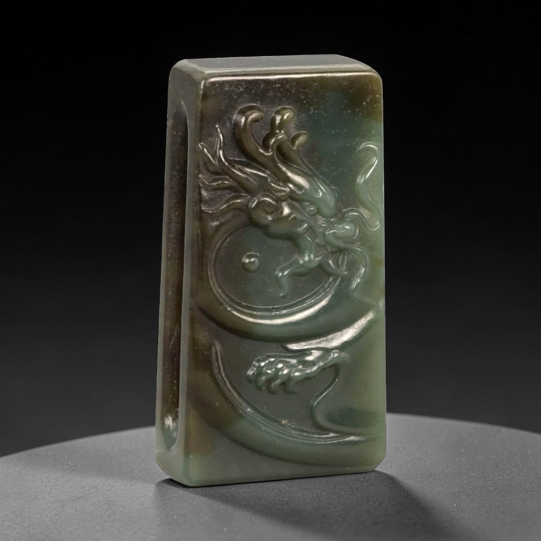 A Chinese Nephrite Jade Belt Buckle, 20th Century, 50FA: Carved from dark green nephrite jade with areas of mottled brown and olive tonal variation, the buckle is rectangular in form with slightly rounded edges and a flat reverse. The obverse is carved in l