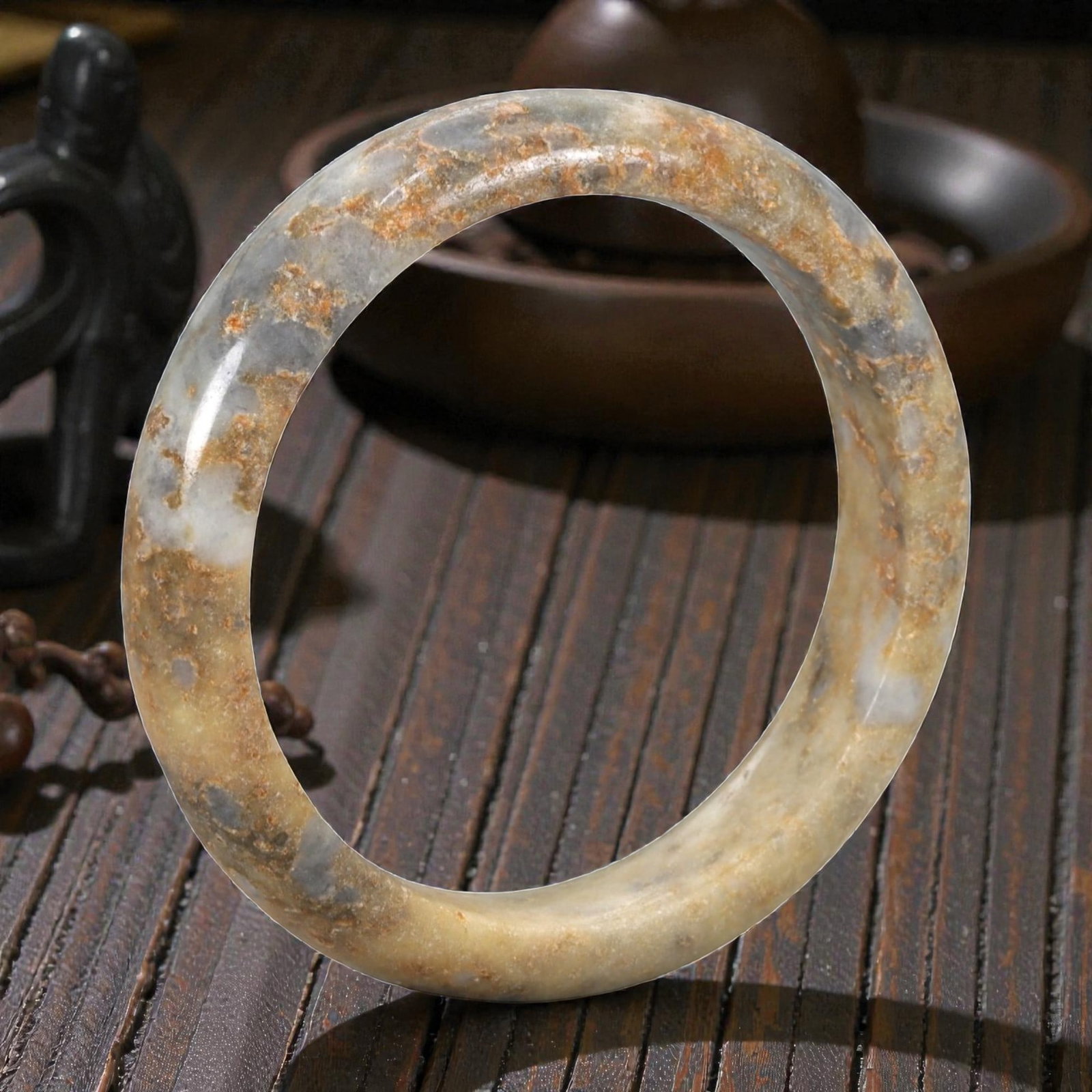 Natural Burmese Type A Jadeite Jade Bangle Bracelet, 20th Century, 100ZK: Carved from jadeite jade with a pale yellowish-tan base and prominent russet and greyish-blue mineral inclusions concentrated along the upper edge, the bangle is formed as a continuous circular band w
