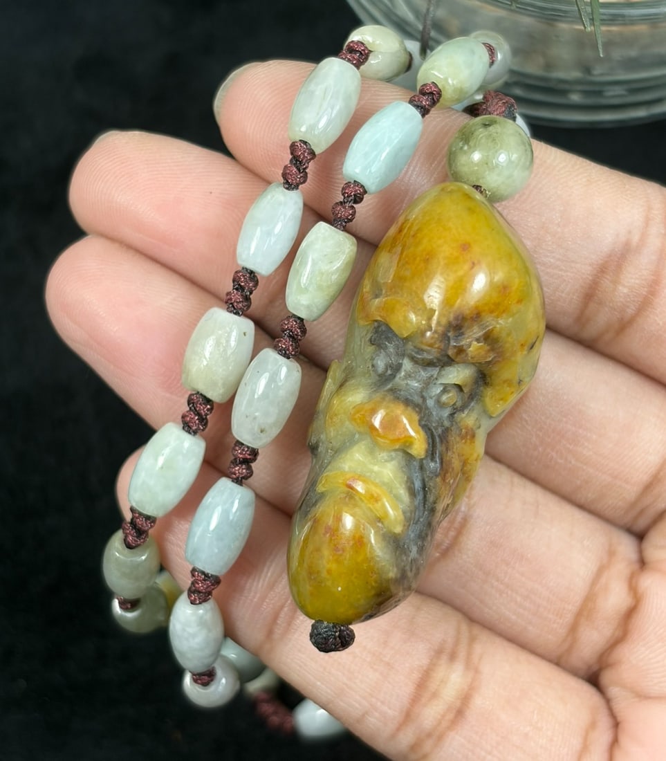 Burmese Jadeite Beaded Necklace with Hetian Jade Luohan Head Pendant, 70YJ: This necklace features a hand-carved Hetian jade luohan head pendant paired with natural Burmese jadeite pebble beads, strung on a brown cord. The pendant is crafted from Hetian jade with rich russet 