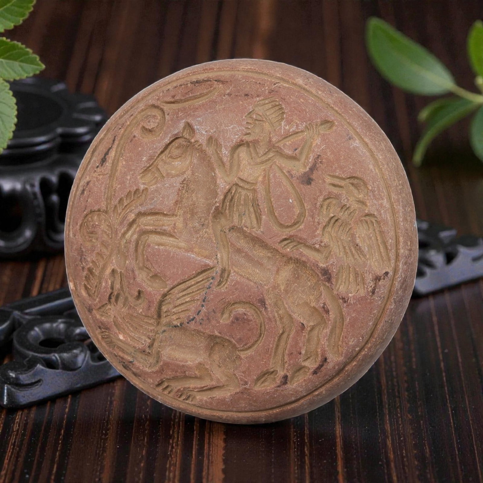 Antique Islamic Steatite intaglio Plaque, 66YD: This antique plaque is carved from reddish-brown steatite, featuring a circular form with a continuous narrative relief scene. The composition depicts a standing figure atop a horse, accompanied by a 