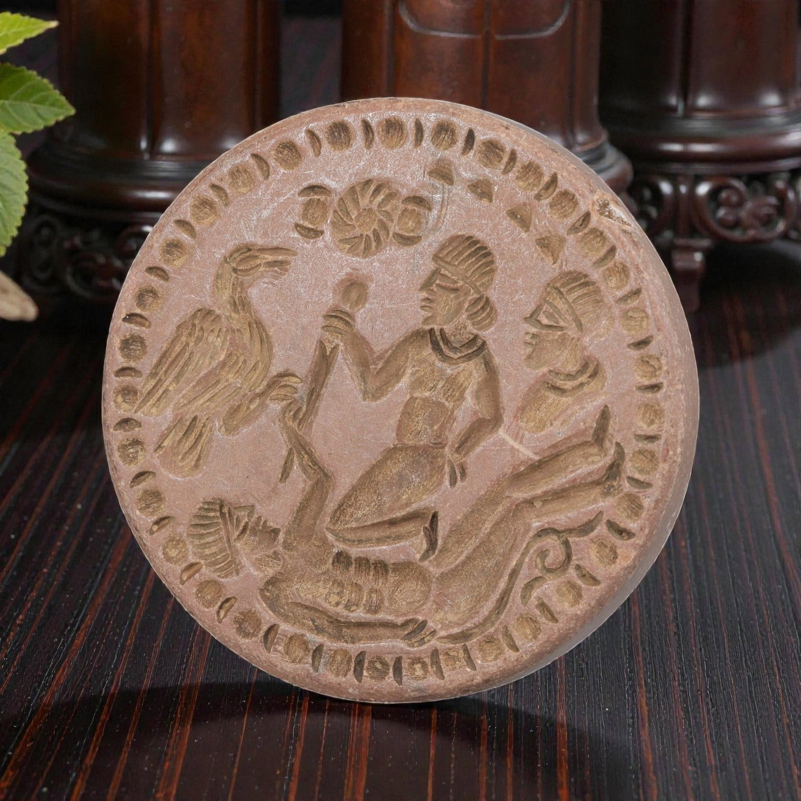 Antique Islamic Steatite Narrative Plaque, 62YD: This antique plaque is carved from reddish-brown steatite, featuring a circular form with a decorative border of incised motifs. The central scene depicts a kneeling figure interacting with a recumben