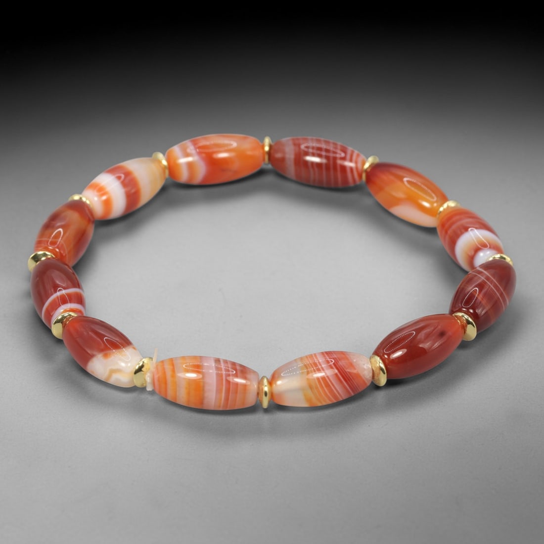 Natural Red Striped Agate Beaded Bracelet - Gold-Tone Spacers, 61XV: This bracelet is hand-strung with natural red striped agate beads, featuring 12 elongated oval beads with unique banded patterns in warm red, orange, and white tones. Each agate bead is separated by s