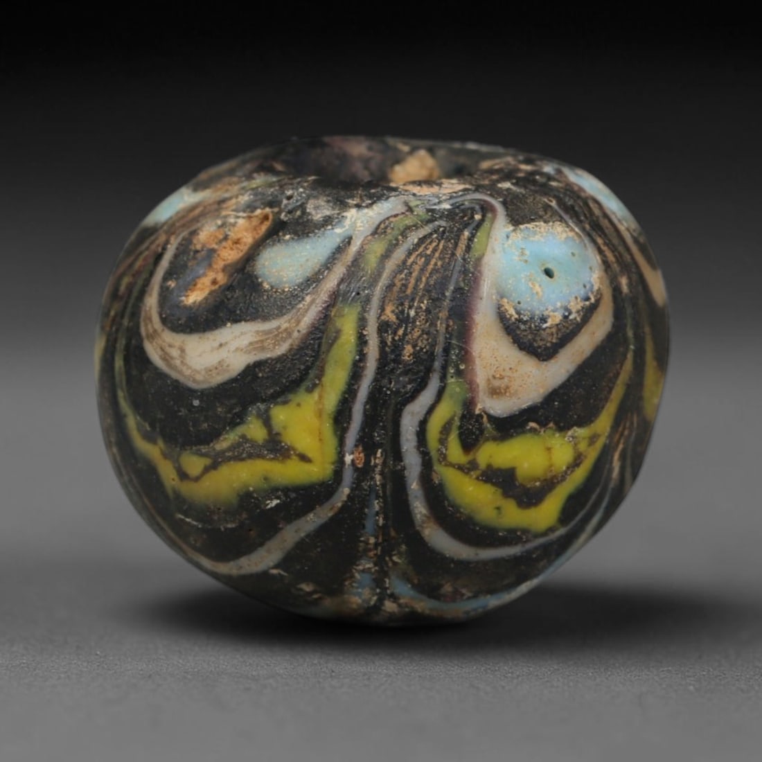 Ancient Islamic Hand Crafted Glass Bead Talisman, 27XD: Miniature antique wearable bead formed from hand-worked glass material, originating from ancient Islamic period glassmaking traditions across the Near East and North African cultural spheres. Glass wa