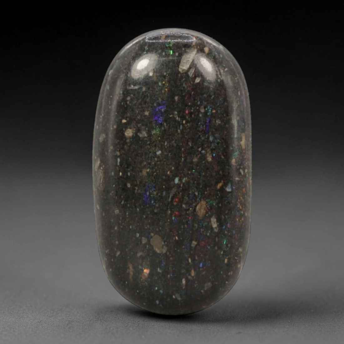 12.26 Carats Australian Matrix Opal Oval Cabochon - Natural Stone, 76XB: This singular oval cabochon matrix opal, measuring 19.8 x 15.2 x 7.1 mm, features a deep, dark host matrix studded with vibrant, scattered opal flecks. The polished surface reveals a dazzling play of 