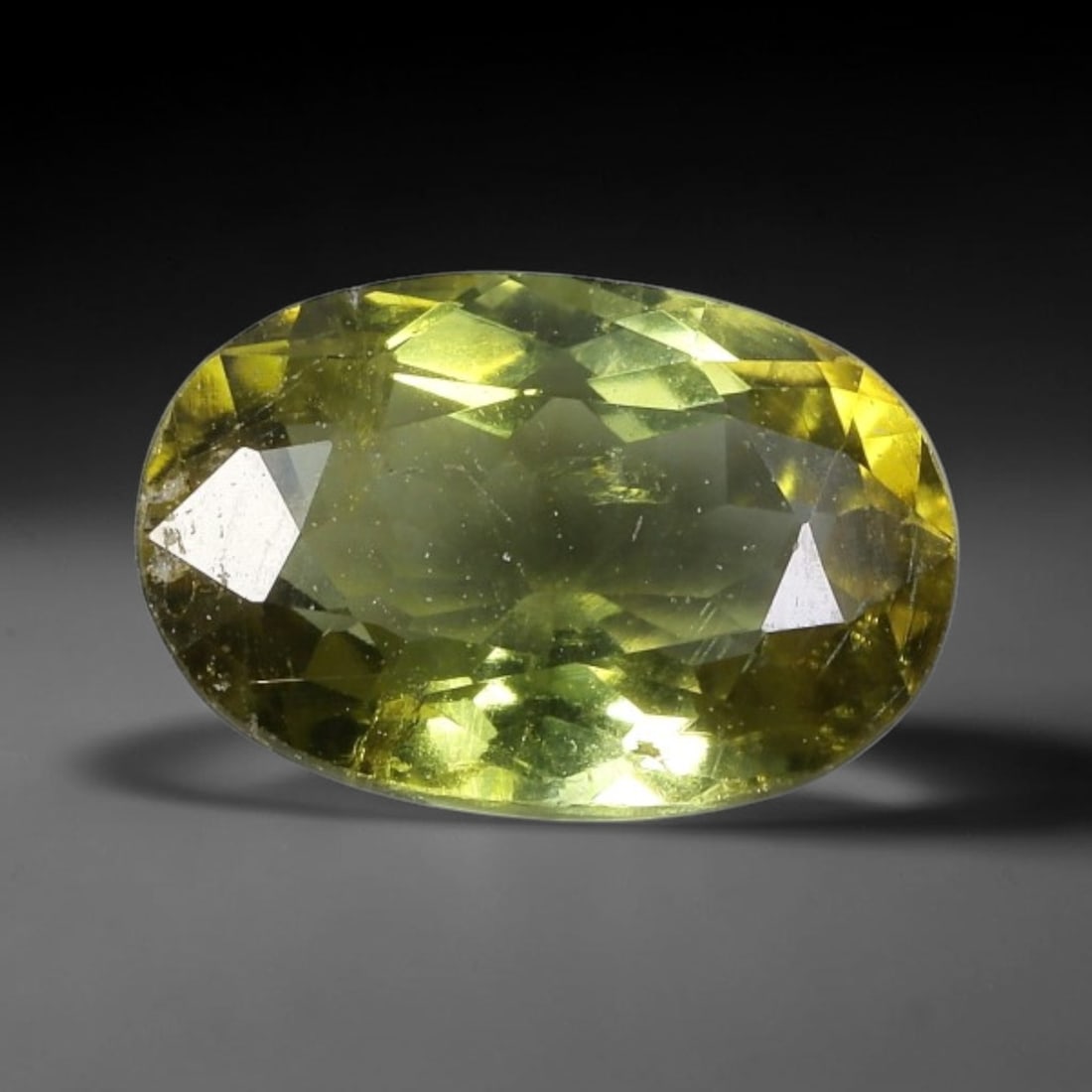 1.45 Carats Olive-Yellow Tourmaline Oval Cut - Natural Loose Gemstone, 63XC: This striking oval-cut tourmaline showcases a rich olive-yellow hue, evoking the warm glow of sunlight filtering through sunlit foliage. Its precision faceting creates a dazzling play of light, with s