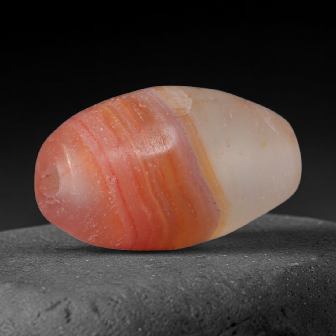Ancient Achaemenid Persian Two-Tone Carnelian Agate Mini Barrel Trade Bead (550-330 BCE), 39XD: This tiny antique dual-toned banded carnelian barrel bead originates from Achaemenid royal hardstone workshops, which produced petite gradient chalcedony talismans for noble everyday adornment and lon