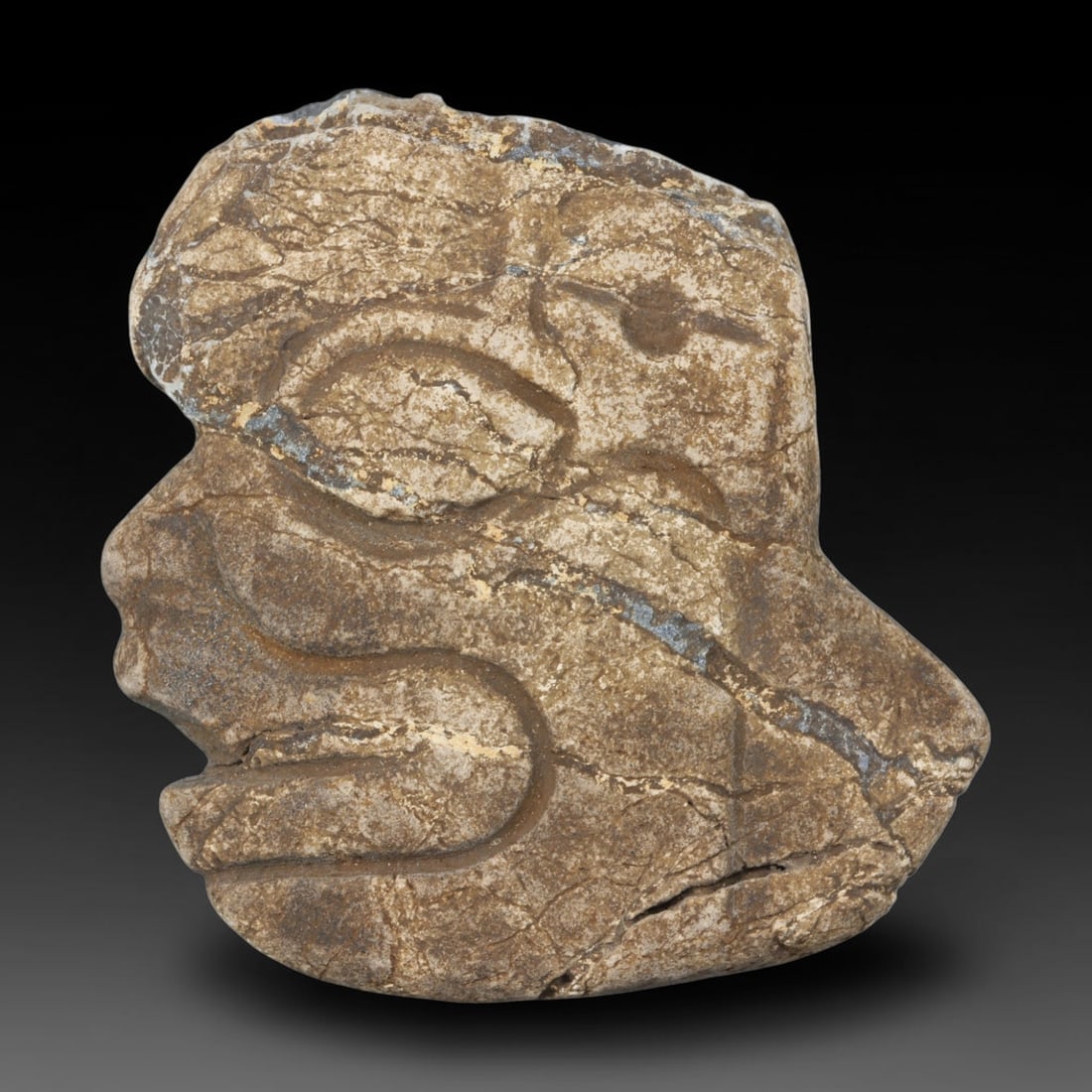 Ancient Medieval Near Eastern Tribal Stone Effigy, 89WT: Carved from weathered natural stone threaded with pale blue mineral veining, this tribal effigy bears a profile human facial form defined by deep incised lines marking the eye, nose, lips and cranial 
