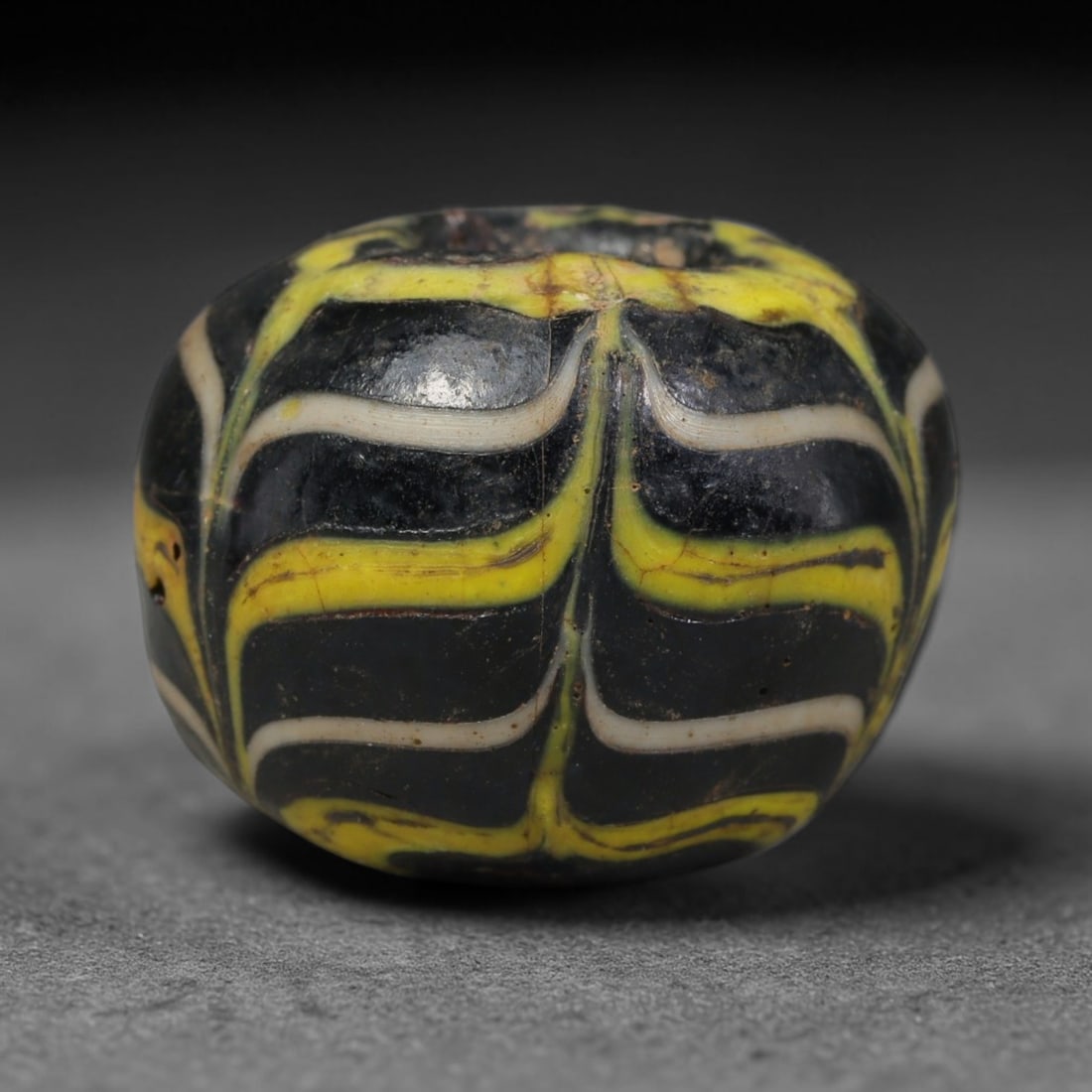 Ancient Islamic Hand Crafted Glass Bead Talisman, 25XD: Miniature antique wearable bead formed from hand-worked glass material, originating from ancient Islamic period glassmaking traditions across the Near East and North African cultural spheres. Glass wa