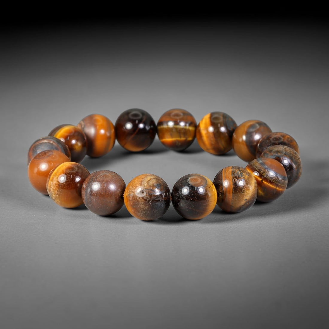 Tiger Eye Bead Bracelet - Polished Natural Stone Jewelry, 60XV: A bracelet composed of polished tiger's eye beads, exhibiting a rich chatoyant banding in golden brown, deep brown, and near-black tones. The beads are generally spherical with minor natural variation